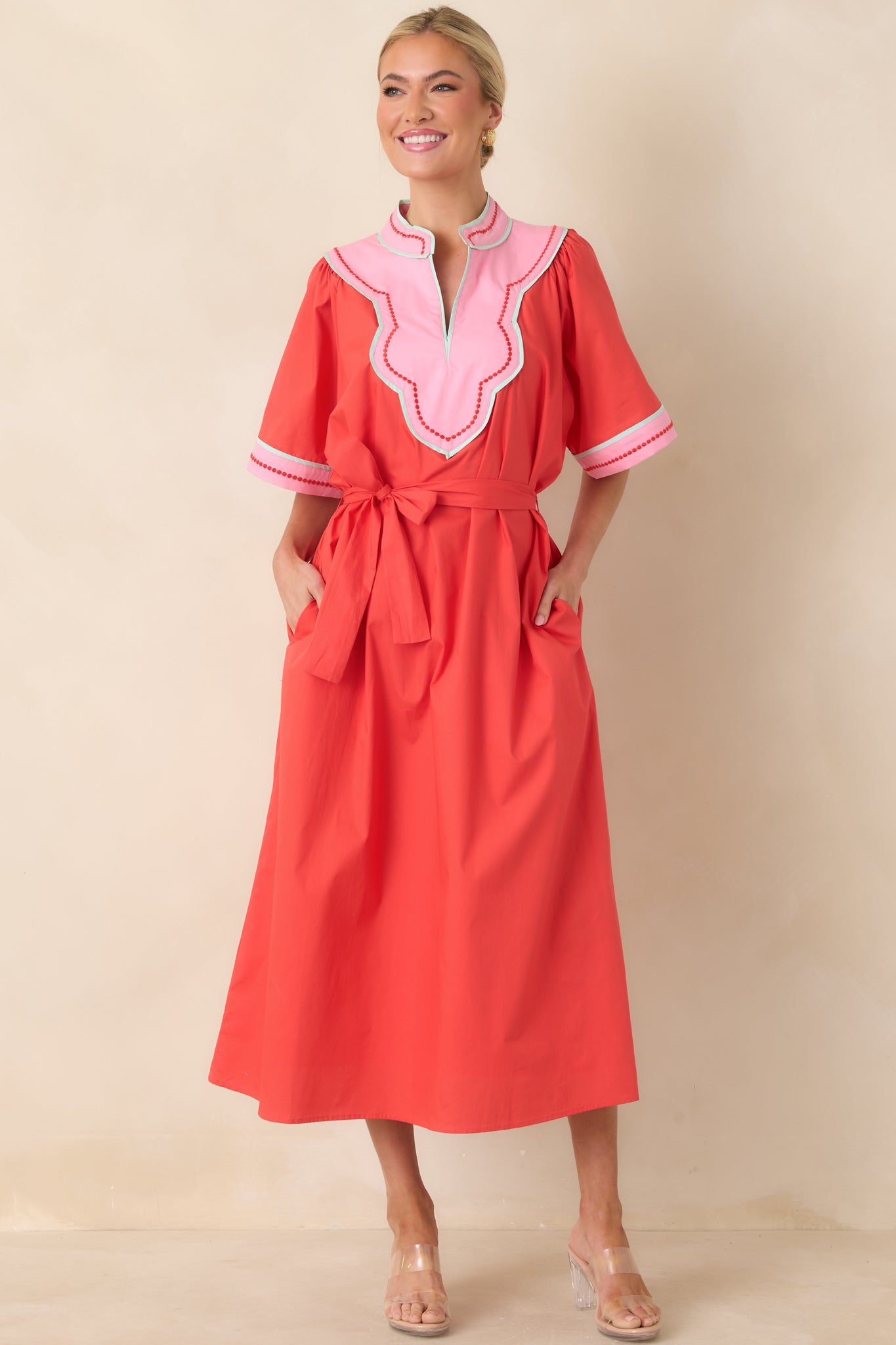 Bold red and pink trimmed midi dress featuring a scalloped V-neck, short flutter sleeves, and a removable tie belt that enhances the structured yet playful shape.