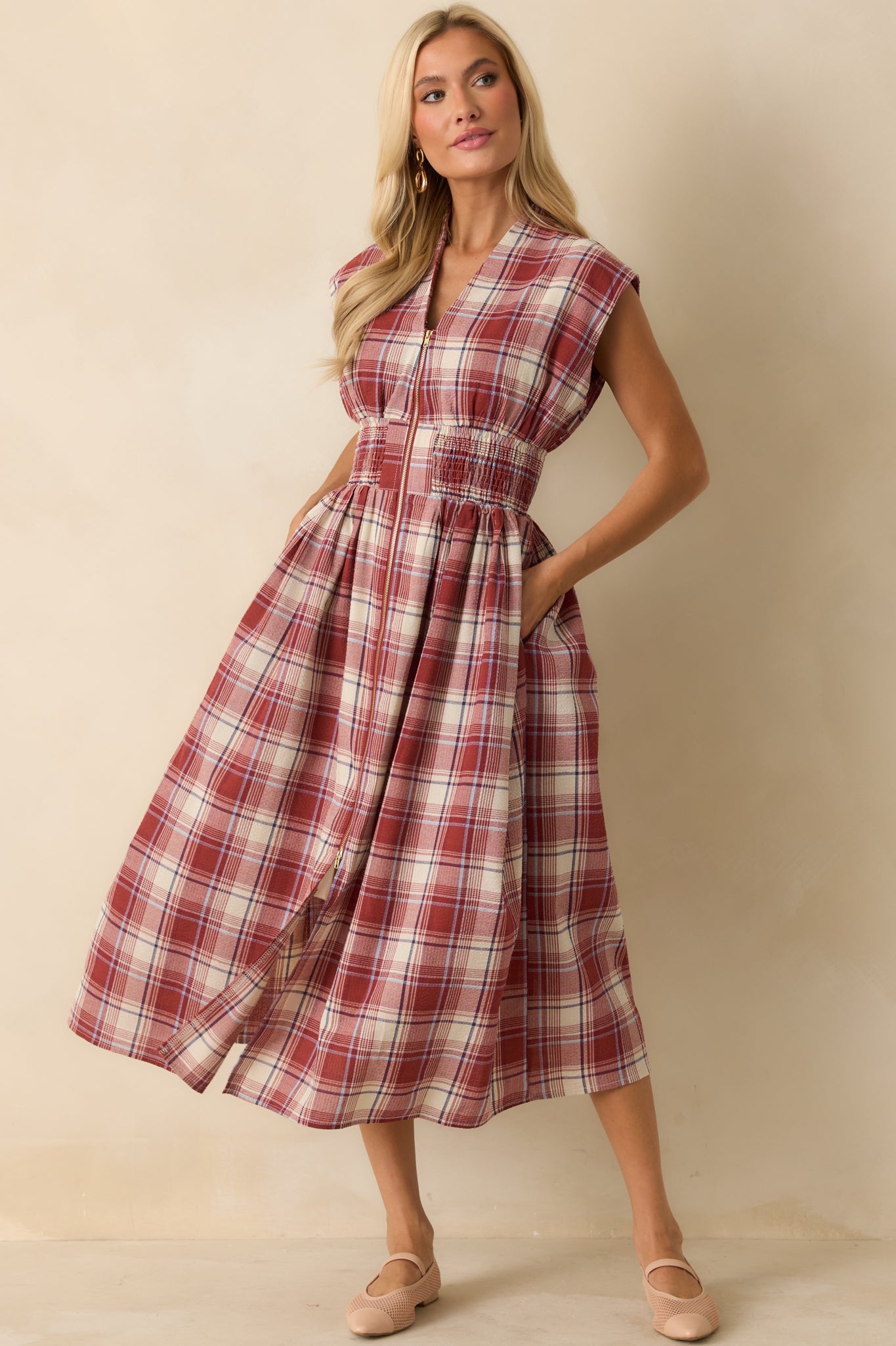 Front view of red plaid midi dress featuring fully smocked waist, functional hip pockets, and flowing skirt with front slit.