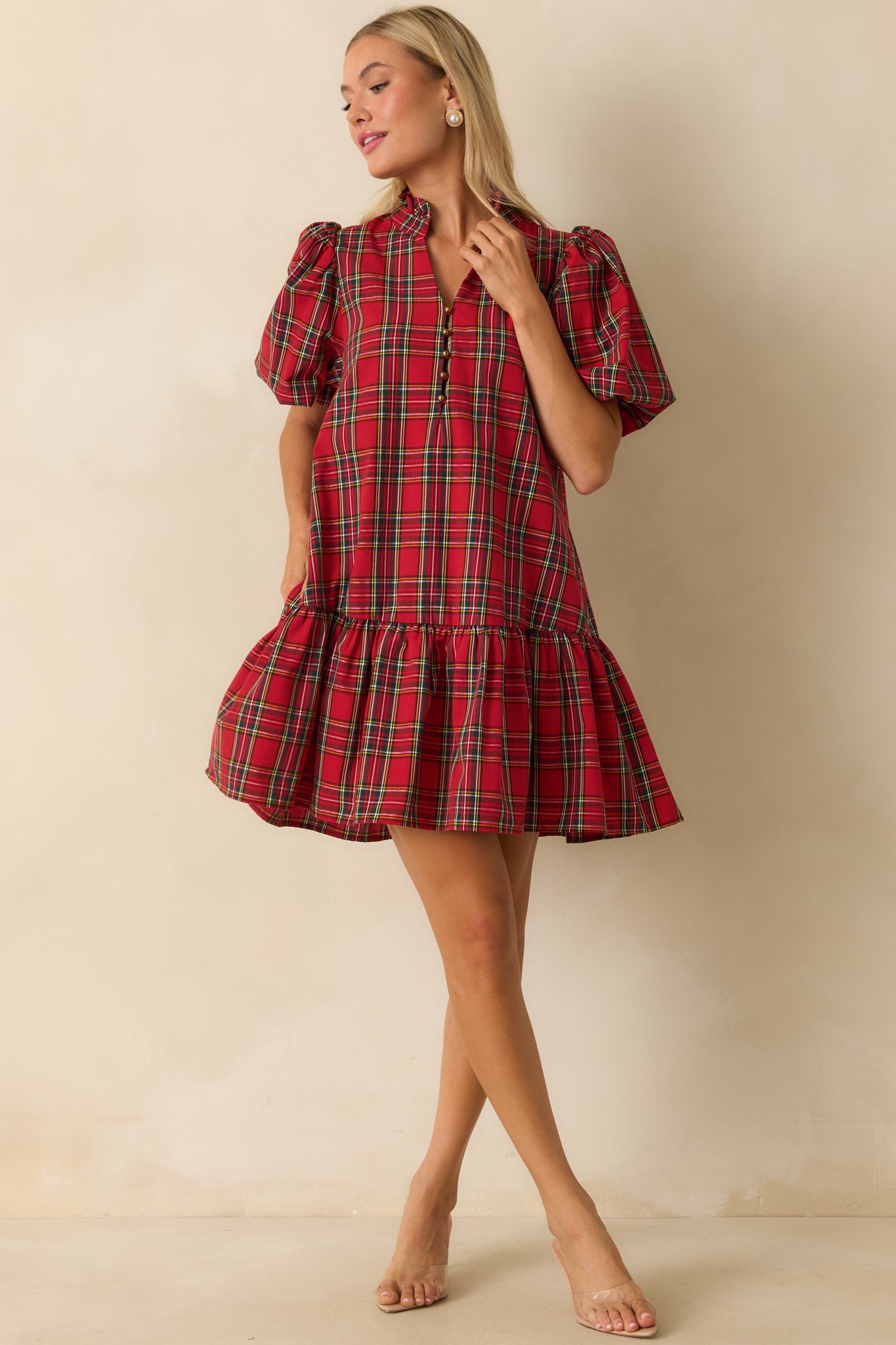 Red plaid mini dress with short puff sleeves, split neckline with button detail, ruffled drop hem, and side pockets.