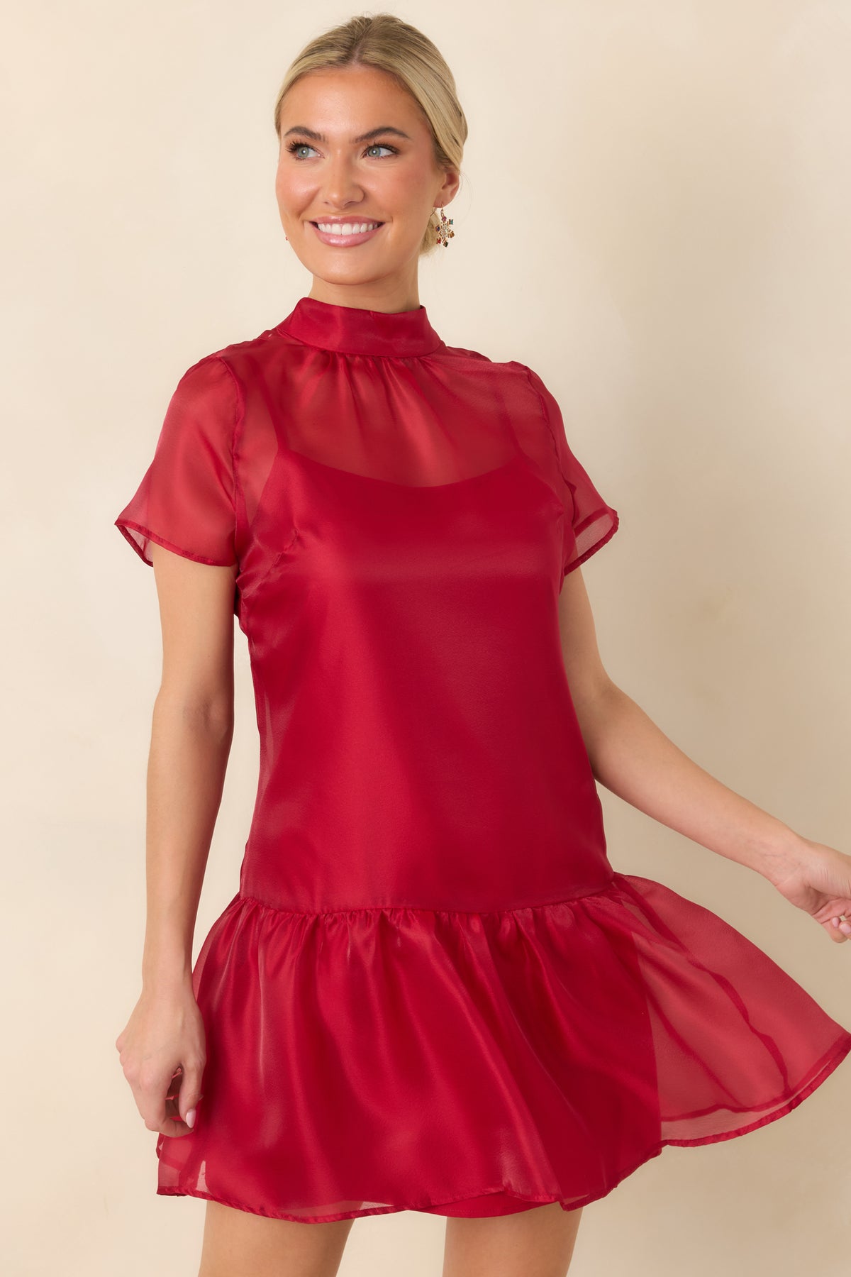 Red dress featuring a sheer upper layer, a softly defined waist, and a gathered ruffle along the hem.