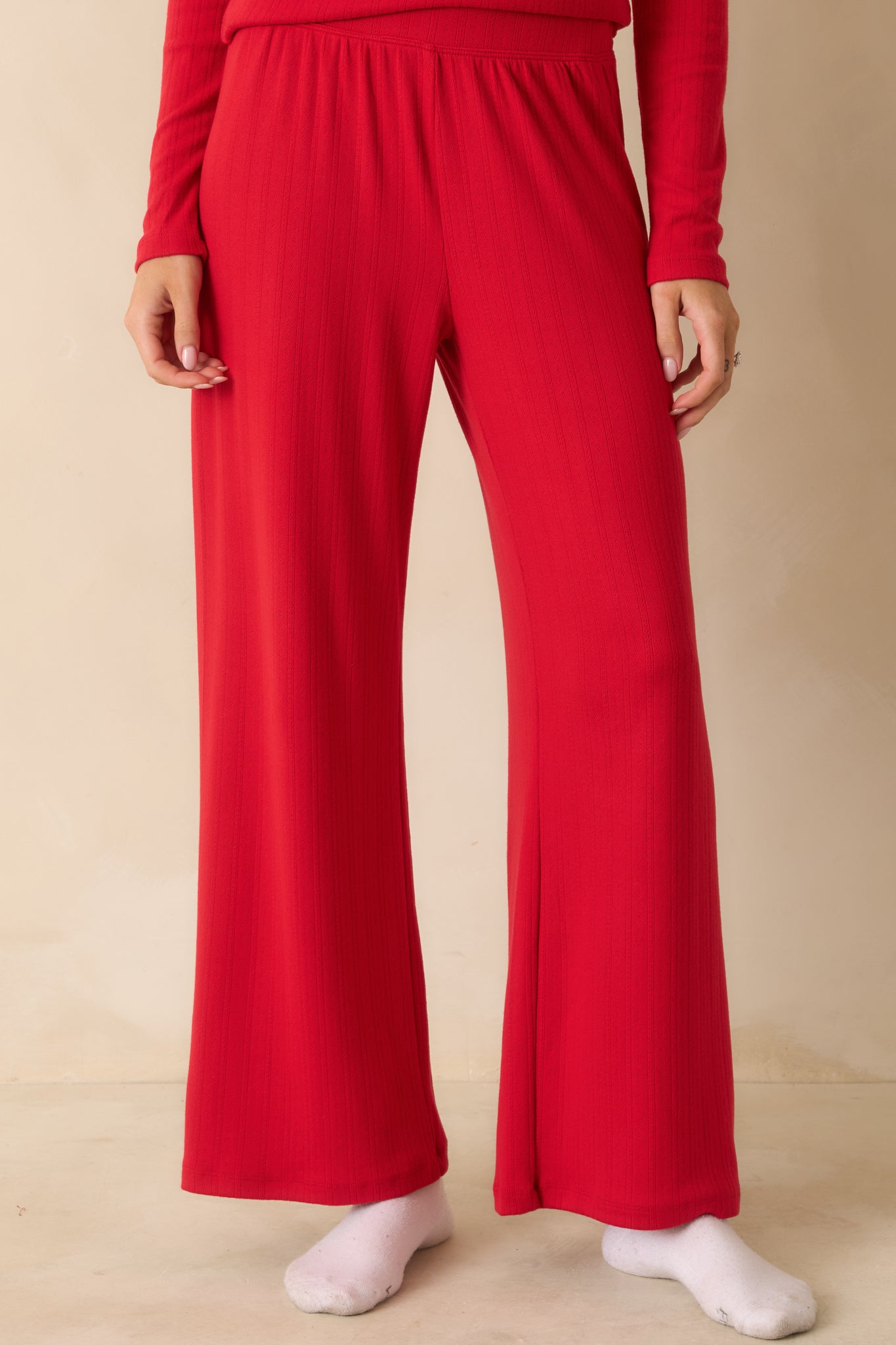 Red wide-leg pants with a high-rise fit, flowing freely to the floor in a silky pointelle knit.