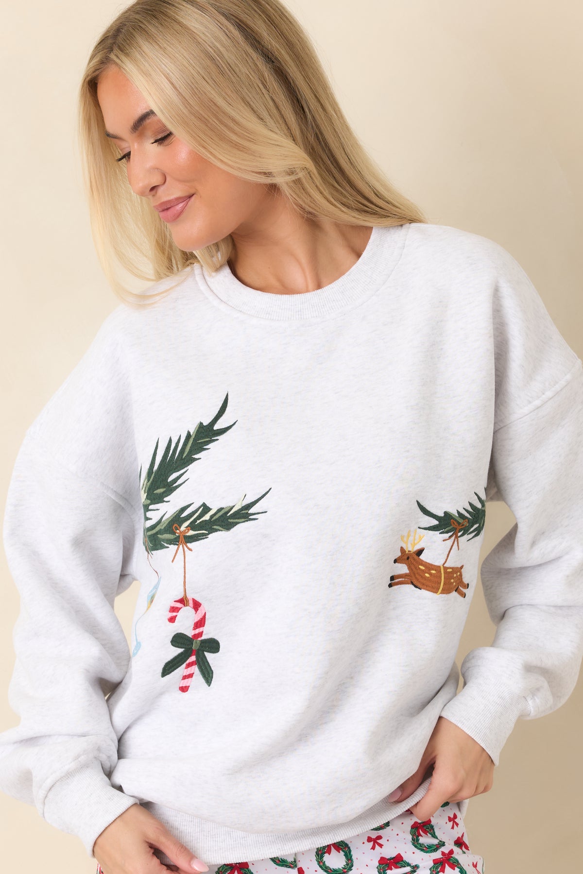 Front of the grey pullover displaying embroidered evergreen branches with a reindeer, candy cane, and festive sweater ornament.
