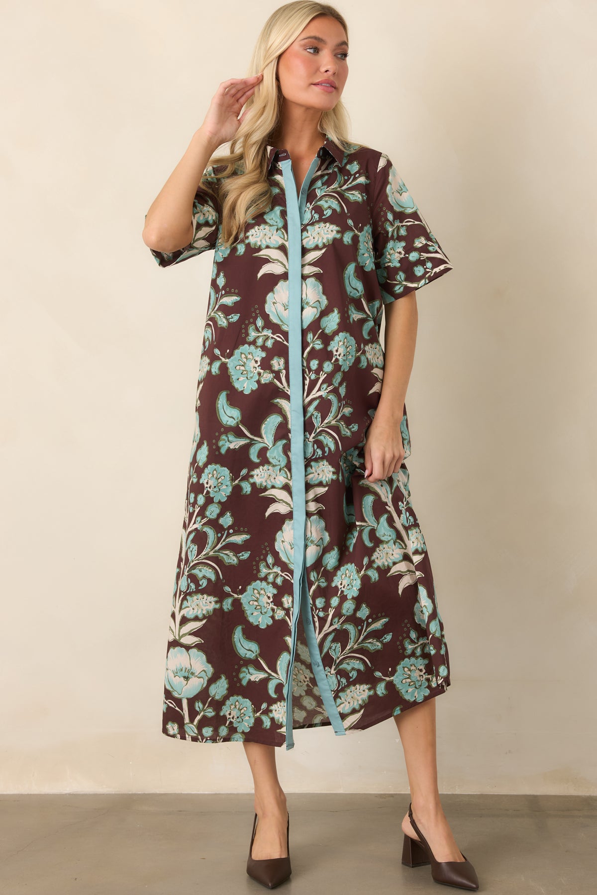 Relaxed botanical dress showcases a pointed collar and aqua contrast placket against the rich brown printed background.
