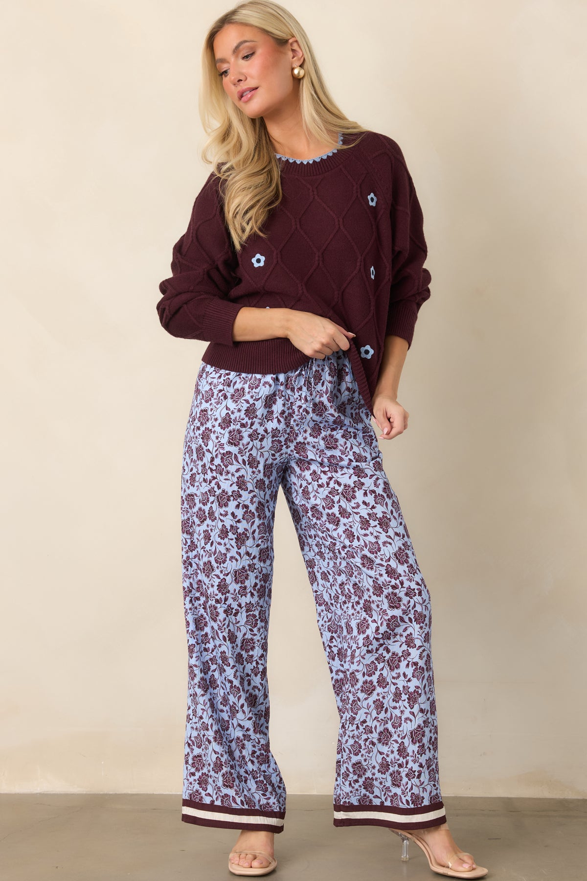 Relaxed floral wide-leg pants with an easy drape, pale lilac background, and bold burgundy and ivory hem stripes.