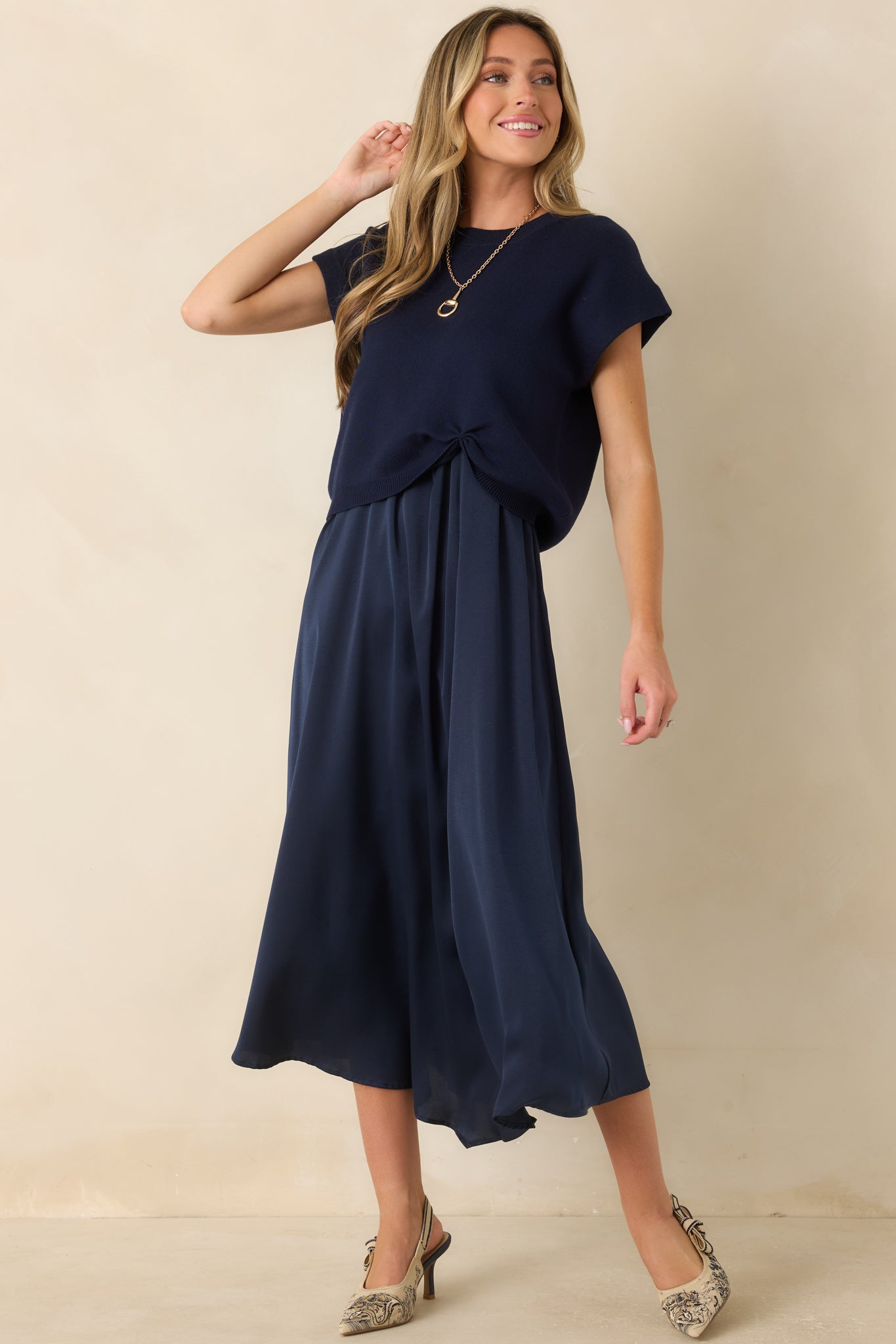 Relaxed navy knit sweater with cap sleeves, a ribbed neckline, soft cotton-acrylic fabric, and a gathered front hem detail.
