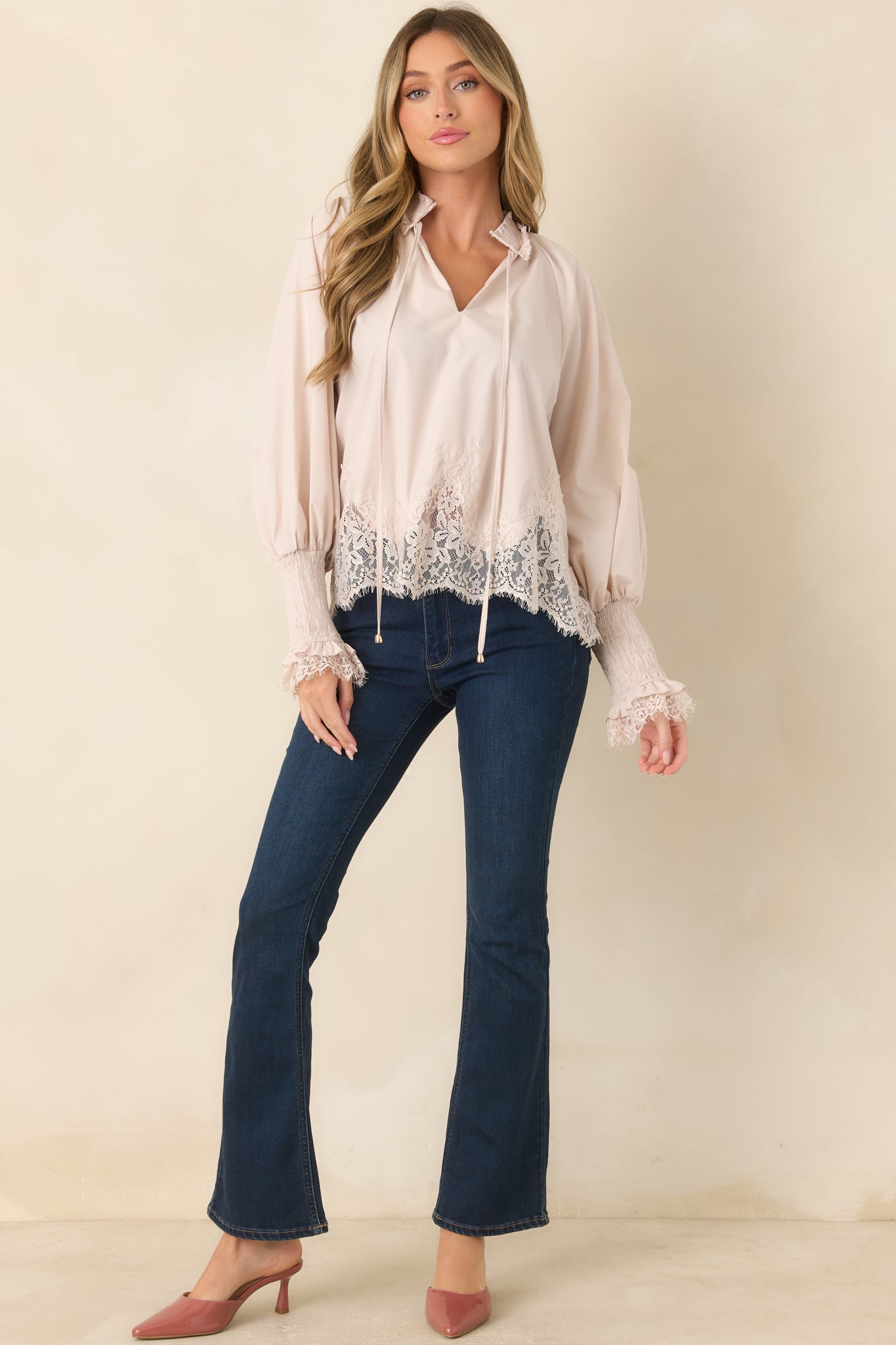 Woven pale neutral blouse combining a relaxed silhouette with a ruffled tie neckline, balloon sleeves, lace-trimmed smocked cuffs, and a decorative floral lace hemline.