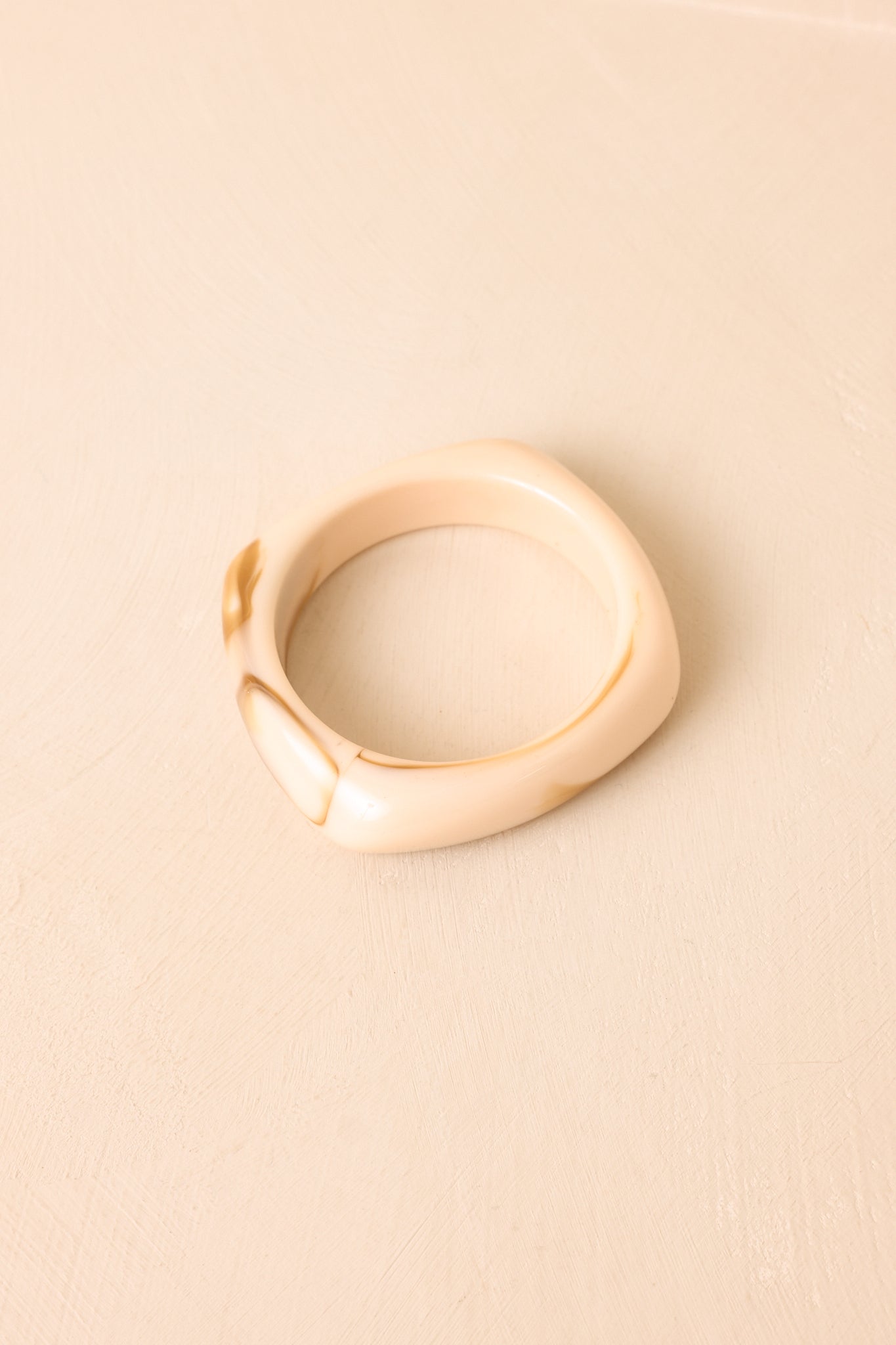 Resin bracelet displayed against a beige background, highlighting its polished surface and sculptural profile.
