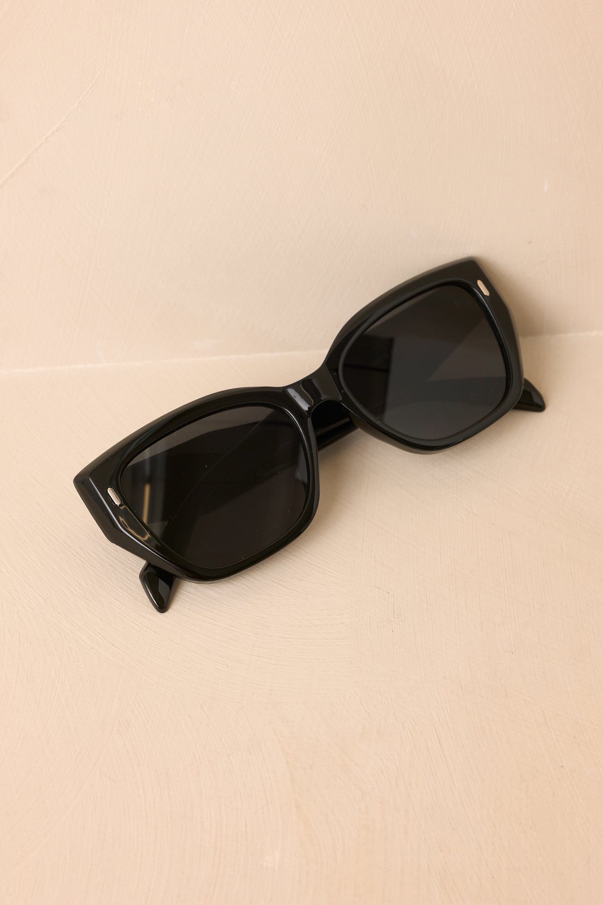 Retro-inspired sunglasses feature a structured black frame, dark lenses, and a gently upswept silhouette with wide side arms.