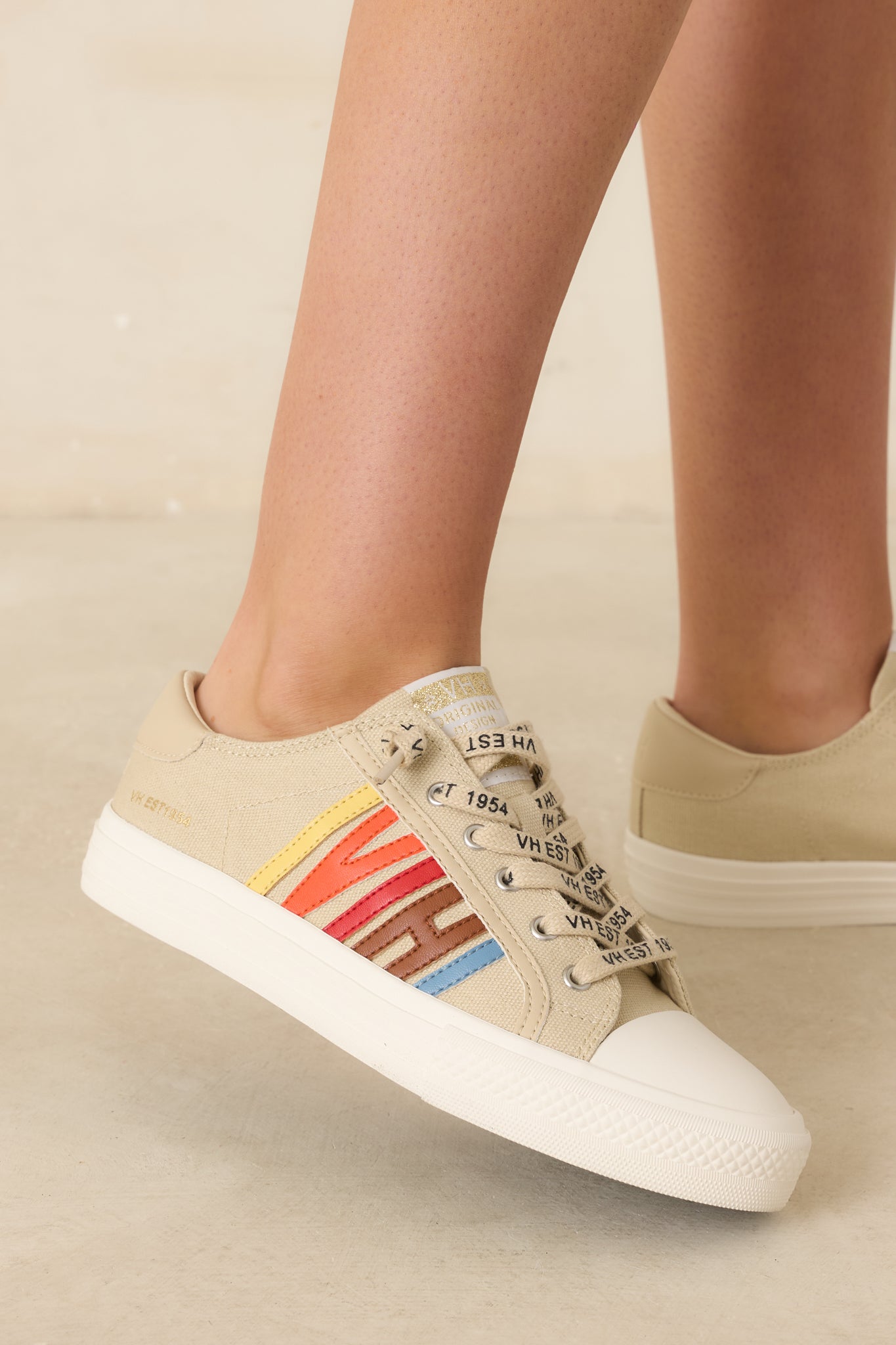 Nude canvas sneakers showcasing retro-inspired yellow, orange, red, brown, and blue side detailing with faux leather heel accents against a beige backdrop.