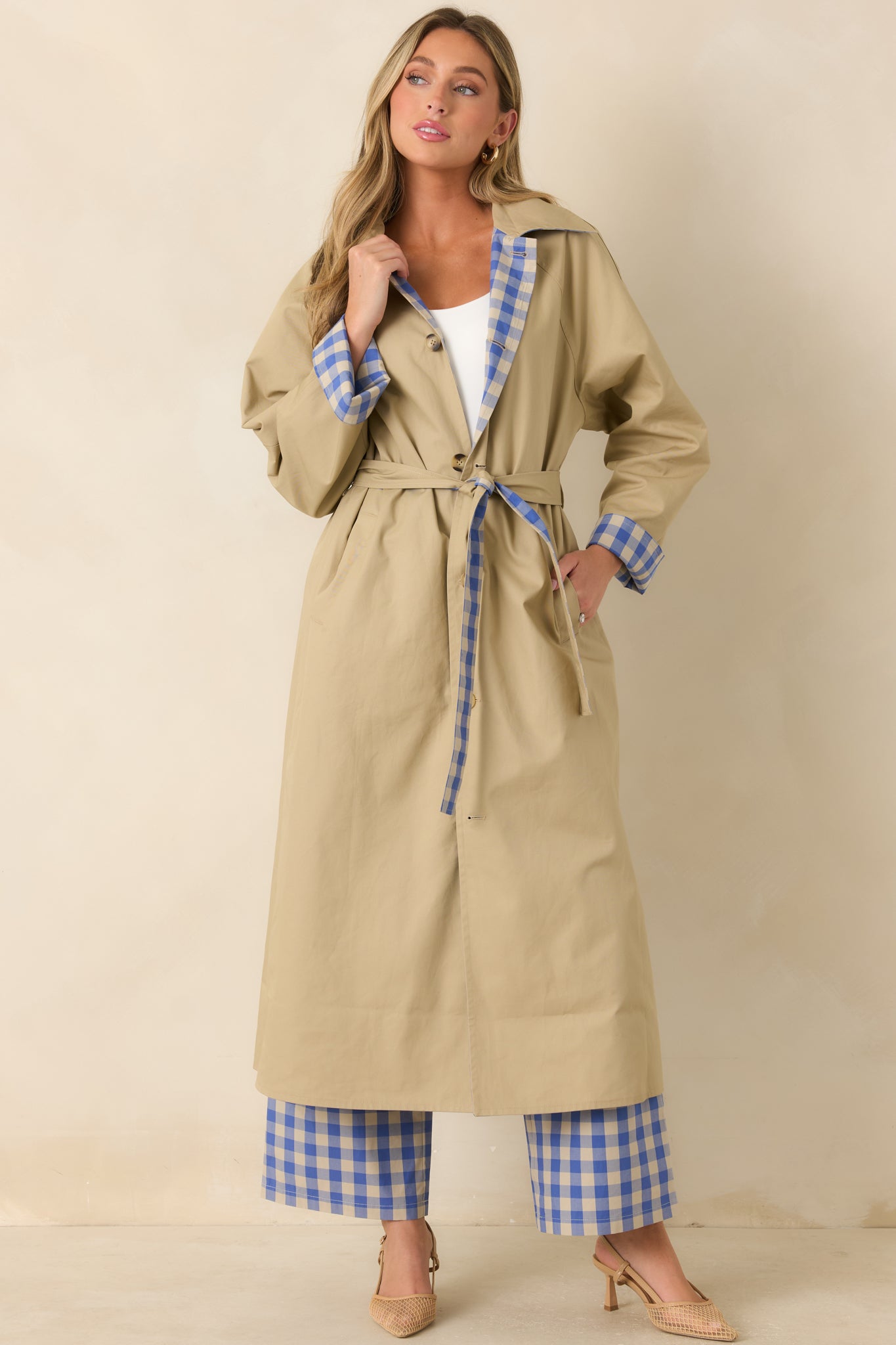 Reversible long coat with the solid beige exterior, featuring a contrasting gingham collar, button-front closure, and adjustable self-tie belt.