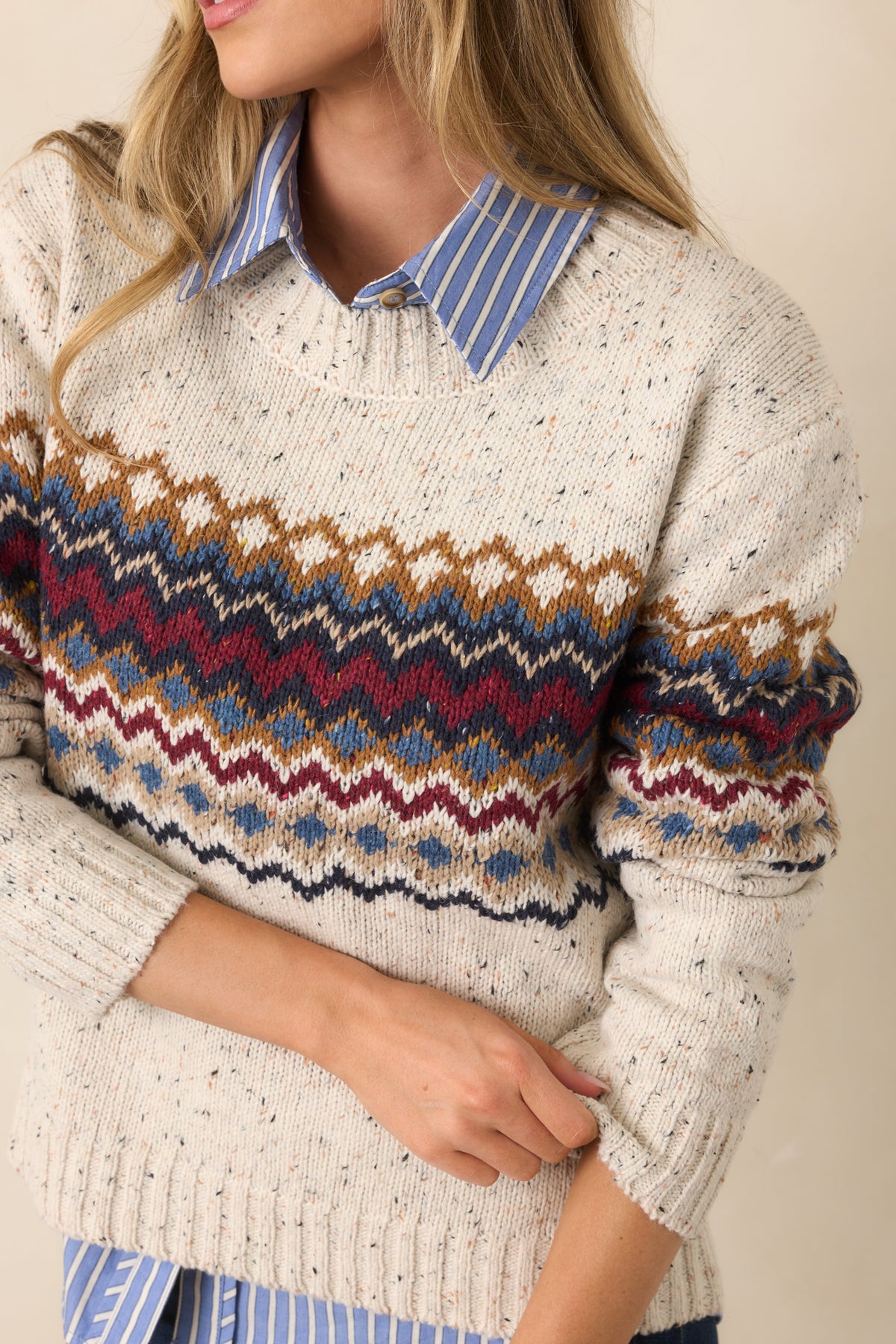 Close-up of the ribbed crew neckline and multicolored burgundy, navy, dusty blue, and camel knit patterning.
