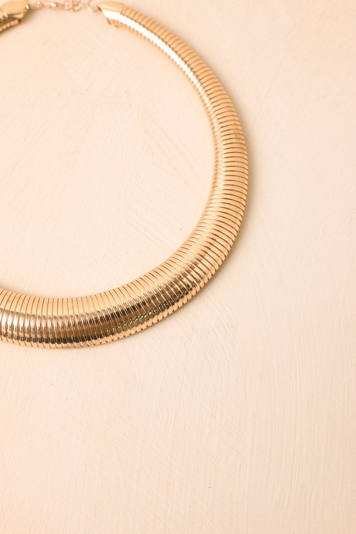 Close-up detail of the necklace highlighting the fine ribbed pattern, reflective gold-tone finish, and sculptural curved construction.