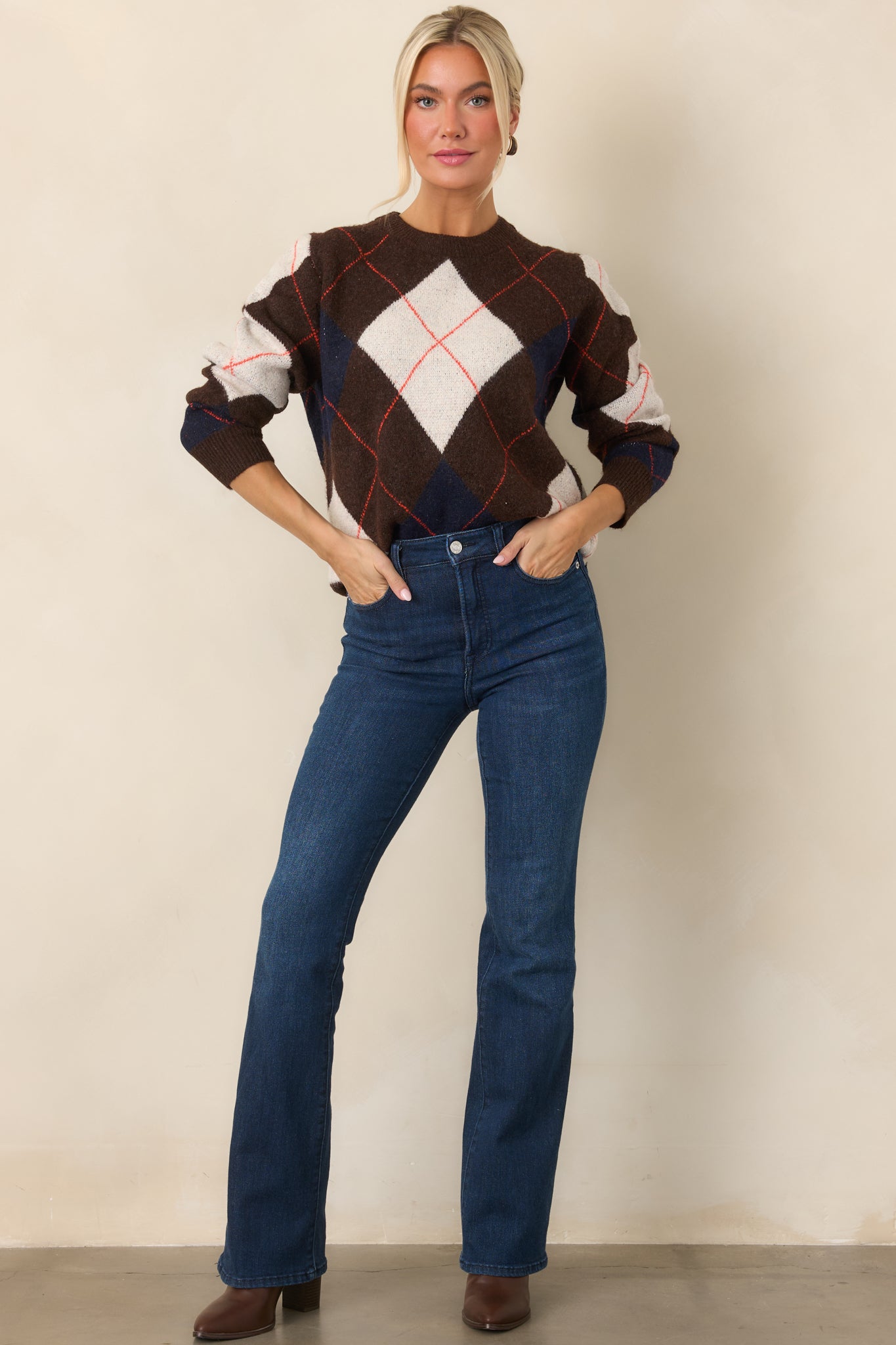Rich brown knit top featuring ivory and navy diamond accents, rust-red lines, and a relaxed silhouette with long sleeves.