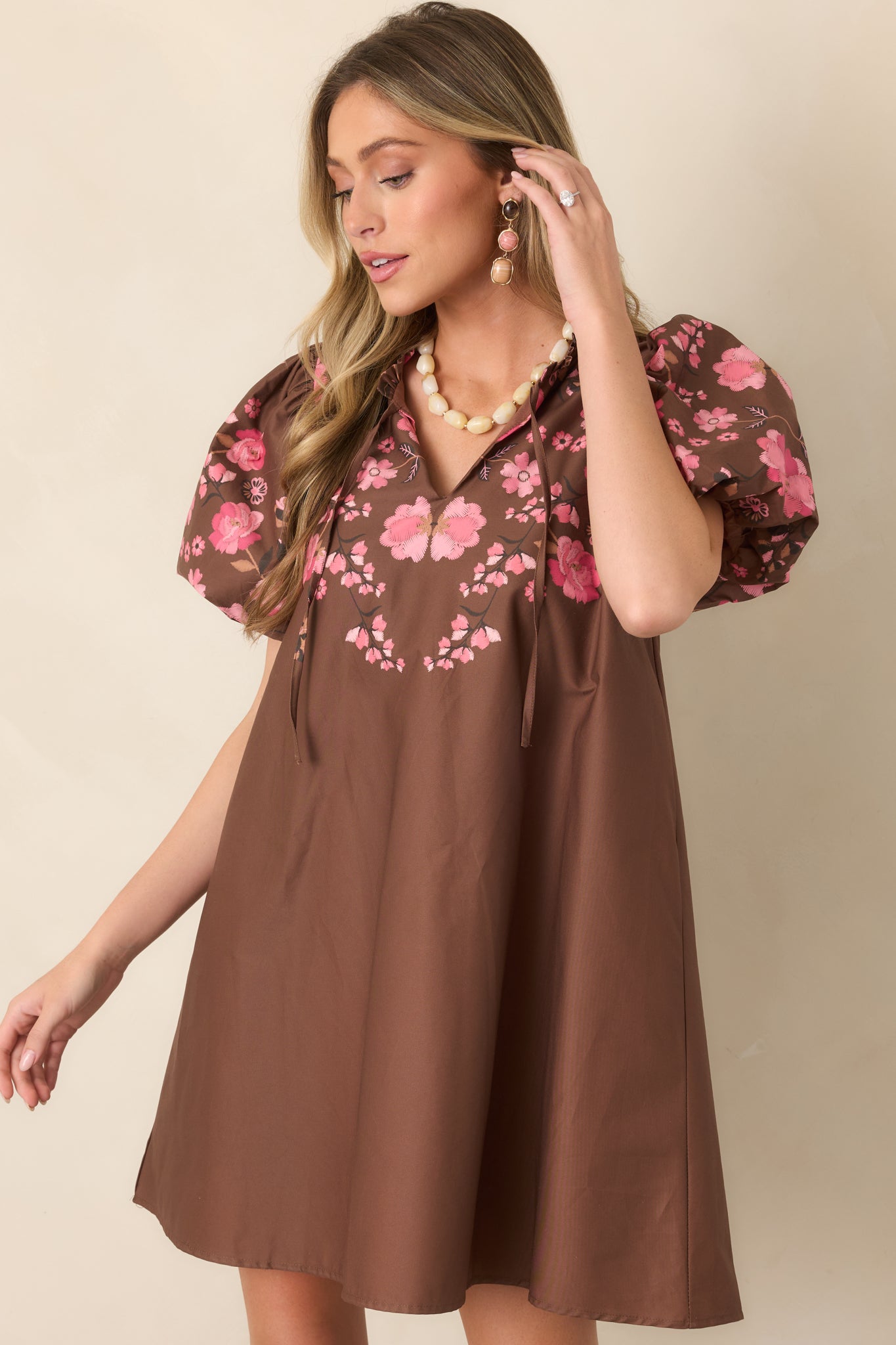 Pink floral detailing stands out against the rich brown fabric of this mini dress, accented by a softly ruffled collar.