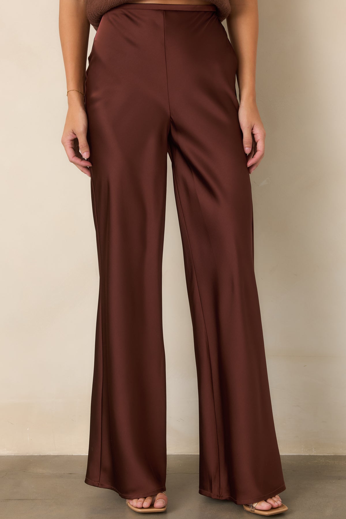 Rich brown satin pants showcasing the smooth high-rise waistband, subtle sheen, and fluid wide-leg construction.