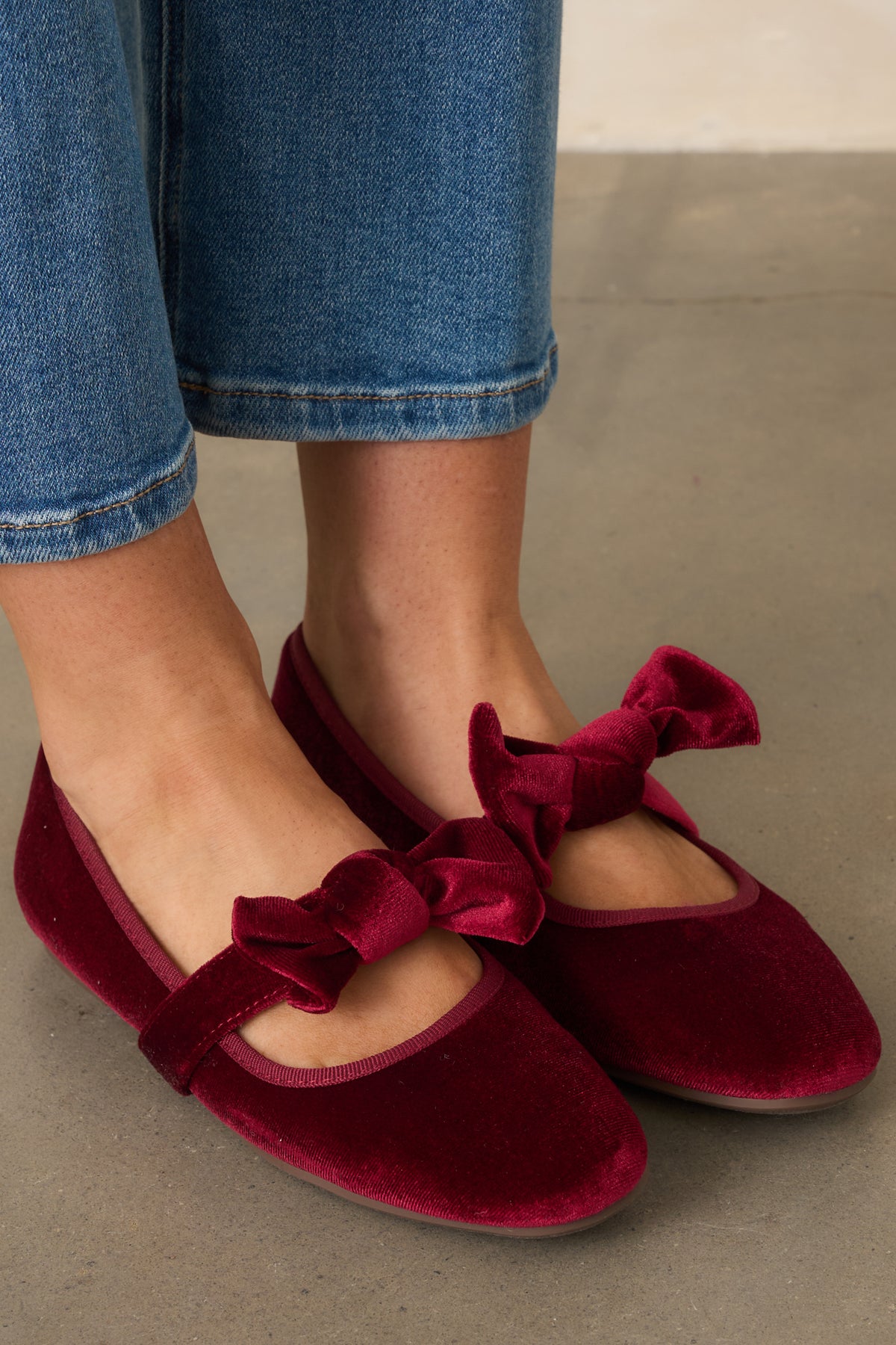 Rich burgundy velvet flats feature a rounded toe and bow-accented Mary Jane strap.