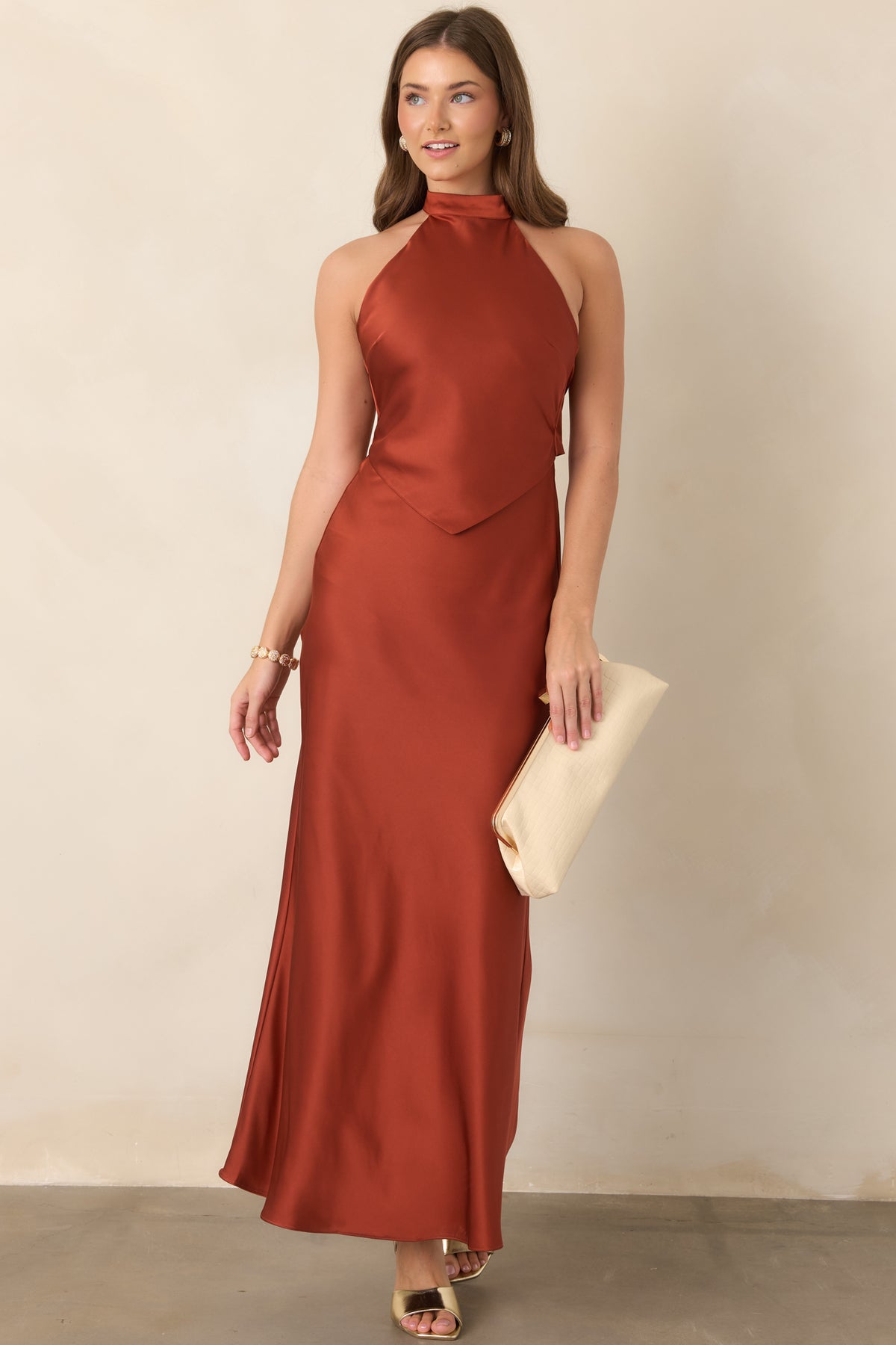 Rich sienna satin maxi dress highlighting its elongated silhouette, sculpted halter neckline, pointed bodice detail, and graceful drape.