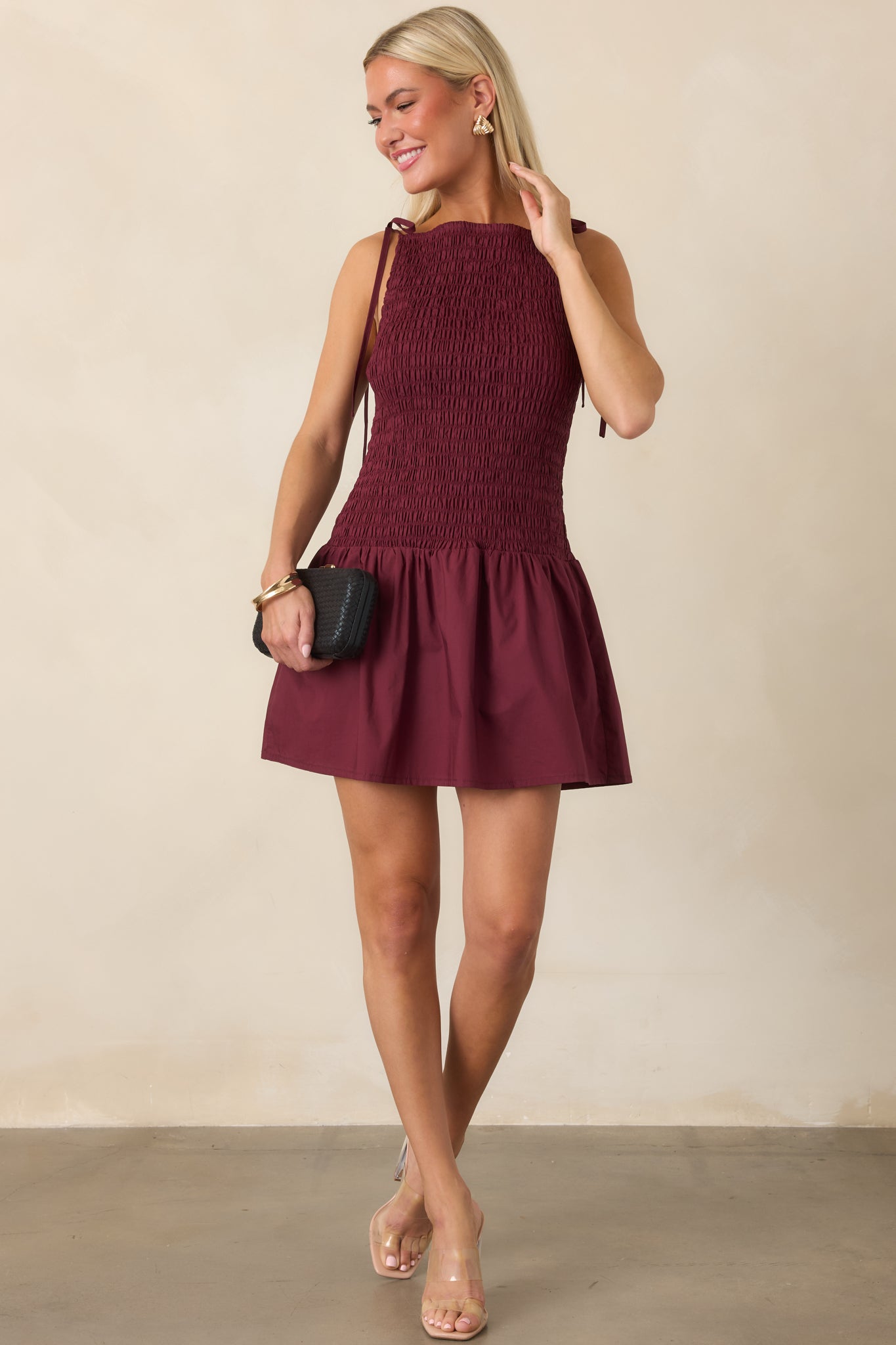 Rich wine red mini dress showcasing its close-fitting shirred bodice, delicate tie straps, gathered skirt, and relaxed flared silhouette.
