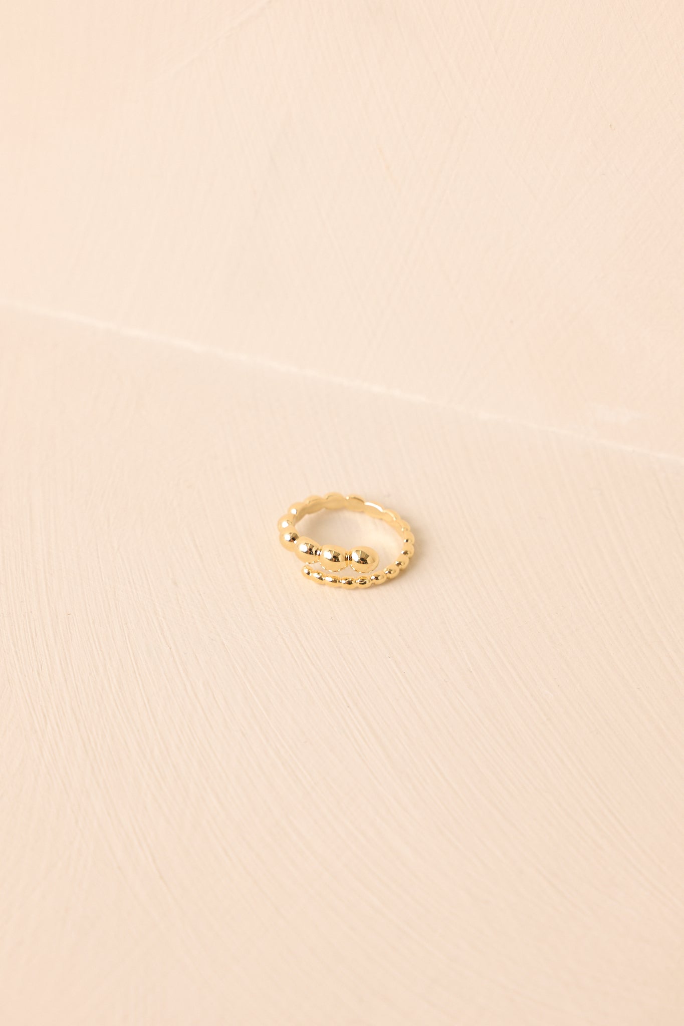 Flat lay of the ring against a beige background, showing the curved open band and polished finish.
