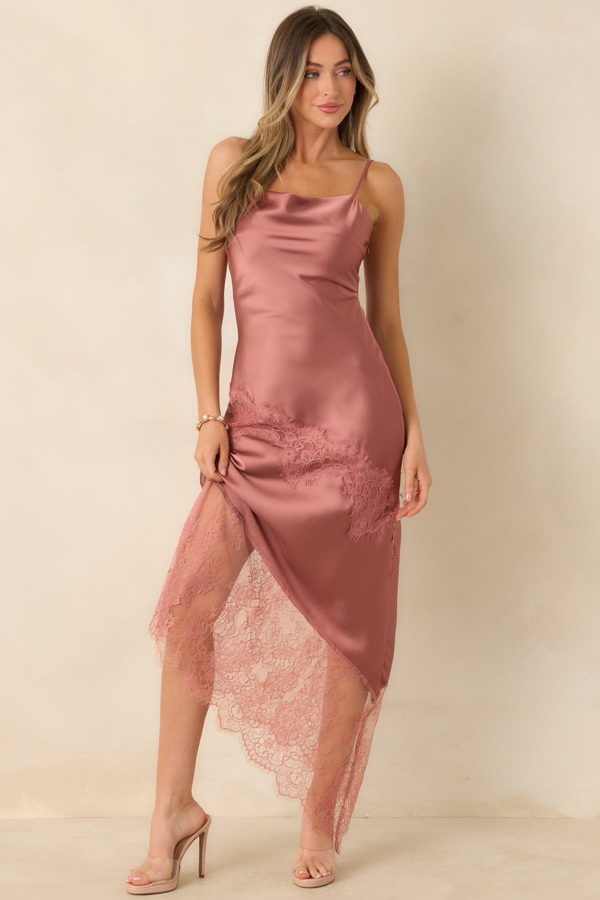Lustrous rose pink satin dress featuring a softly draped neckline and an asymmetric lace-trimmed hem.