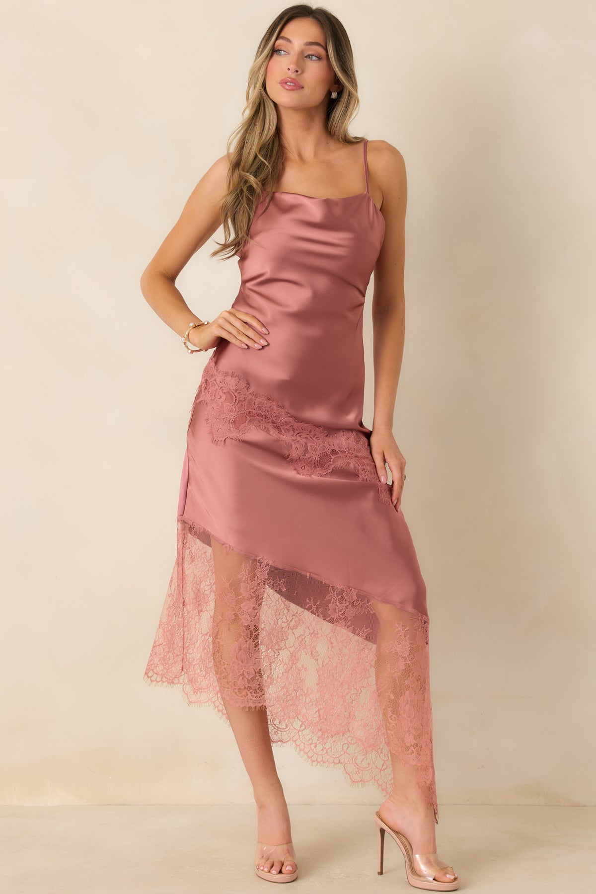 Rose pink satin dress with a draped upper neckline, diagonal lace overlay, and flowing asymmetric hemline.