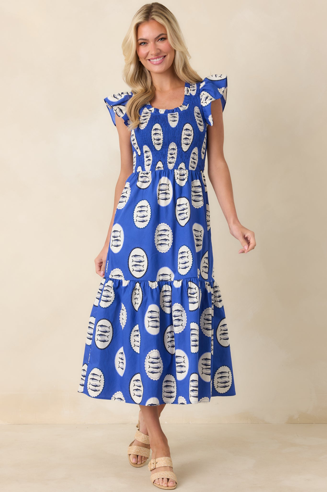 Royal blue cotton dress with an allover playful fish print, featuring a smocked bodice, soft flutter sleeves, and a breezy tiered skirt that flows with easy movement.