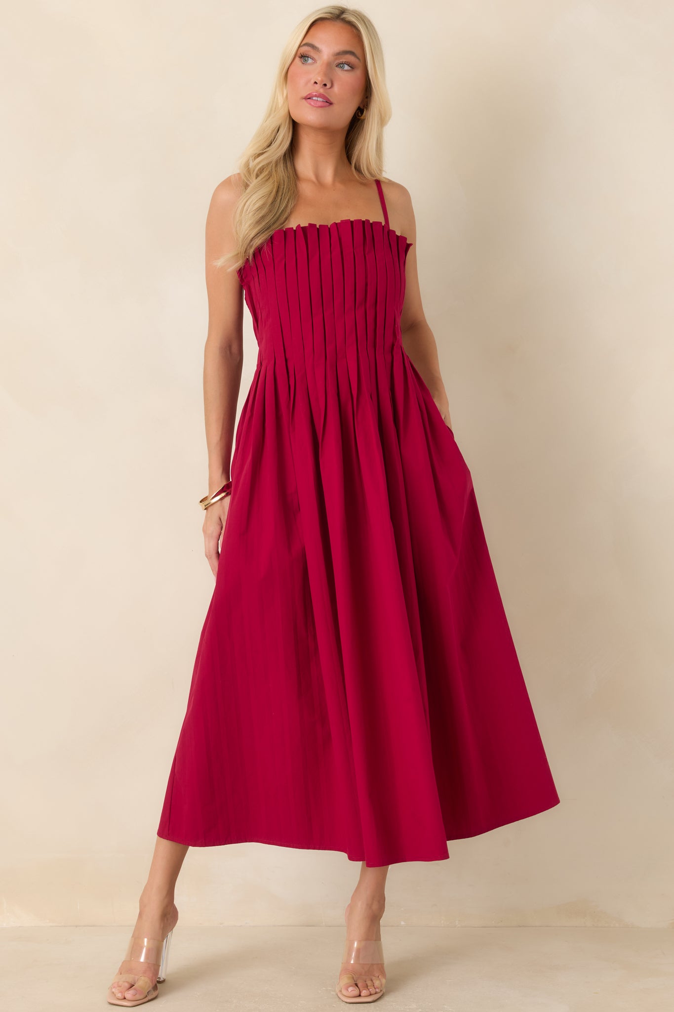Cotton midi dress in a rich ruby red hue showcasing a structured pleated bodice, adjustable spaghetti straps, a gathered waist, and a flowing full skirt.