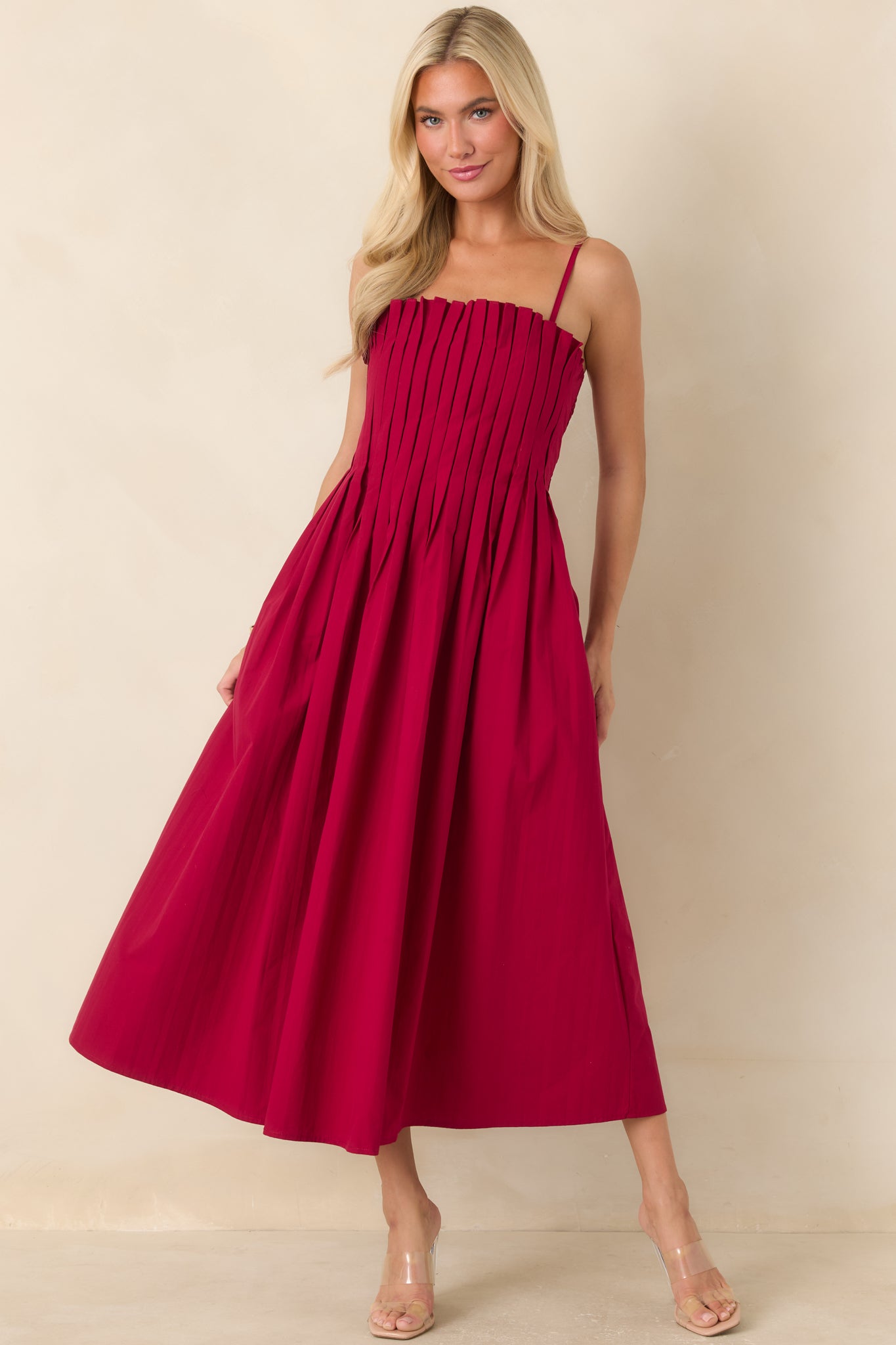 Ruby red 100% cotton midi dress featuring adjustable spaghetti straps, a square neckline, a vertically pleated fitted bodice, and a gathered skirt with side pockets.