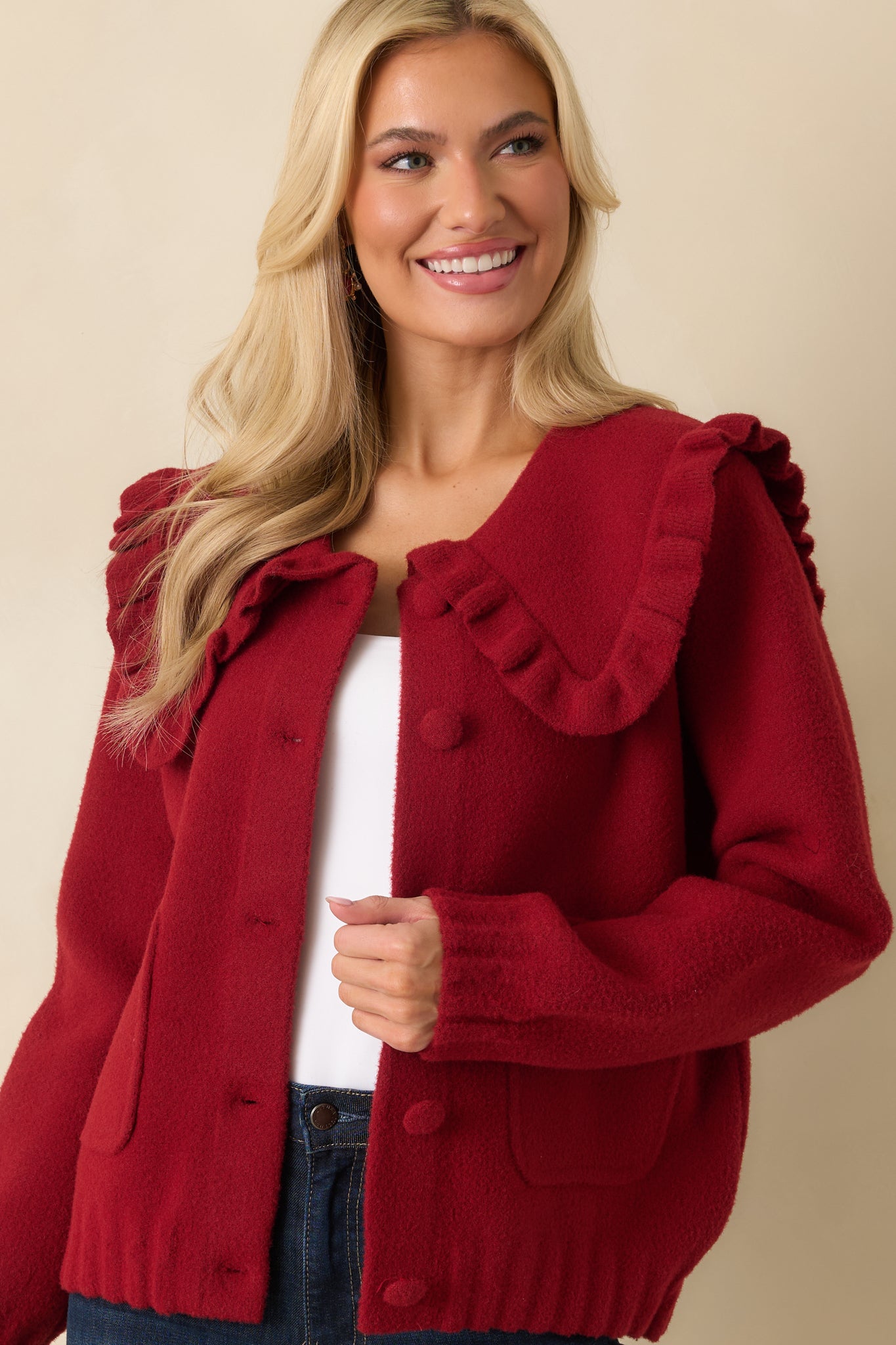 Focused view of ruffle collar and button closure on textured red cardigan.