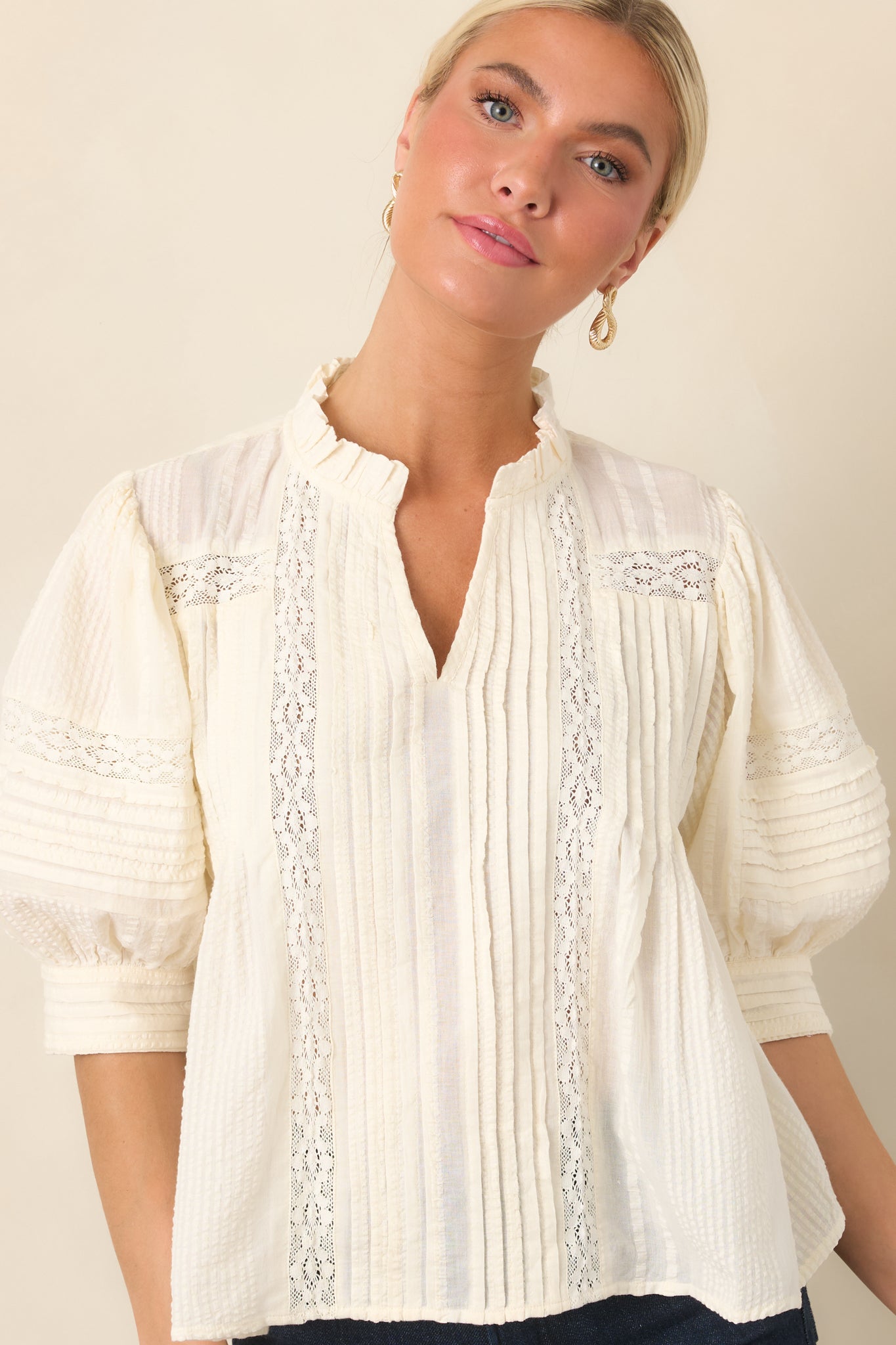 Textured blouse highlighting its softly ruffled neckline, vertical pleated design, and delicate lace panels across the bodice.