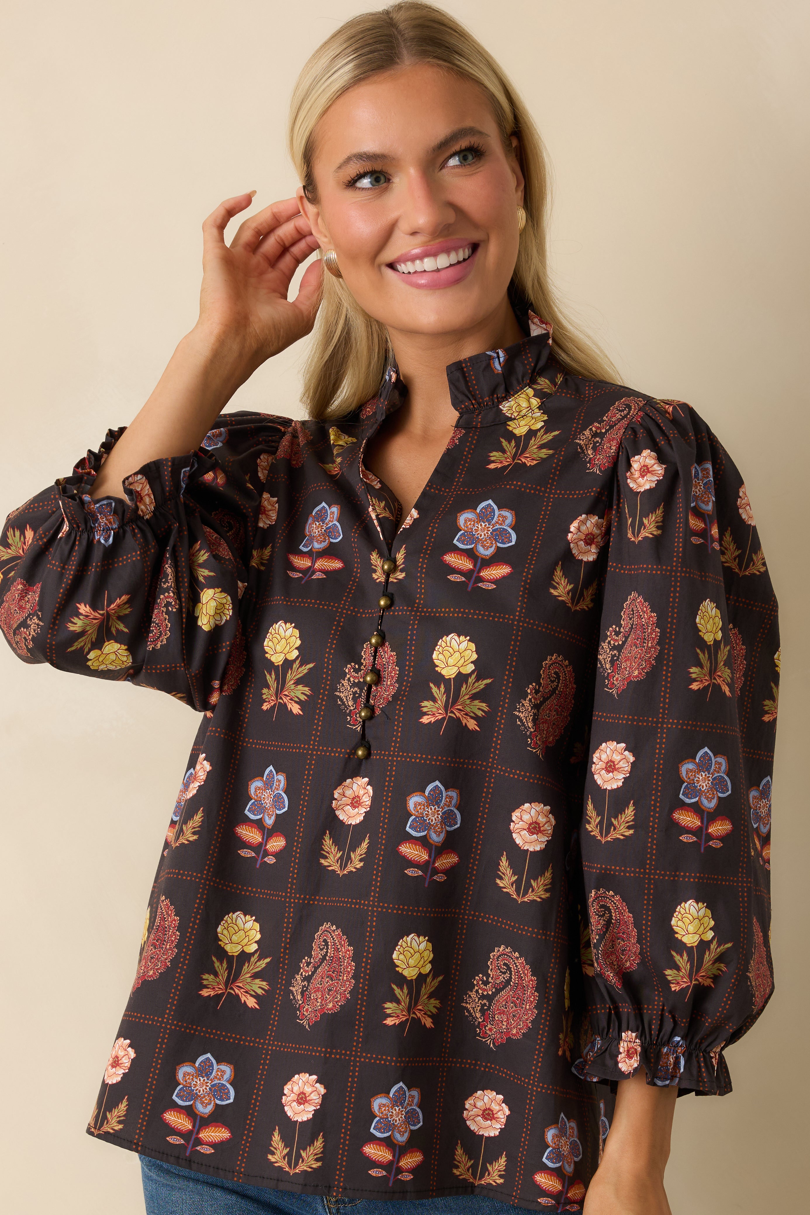 Front view highlighting the ruffled neckline and metallic buttons on the black floral blouse