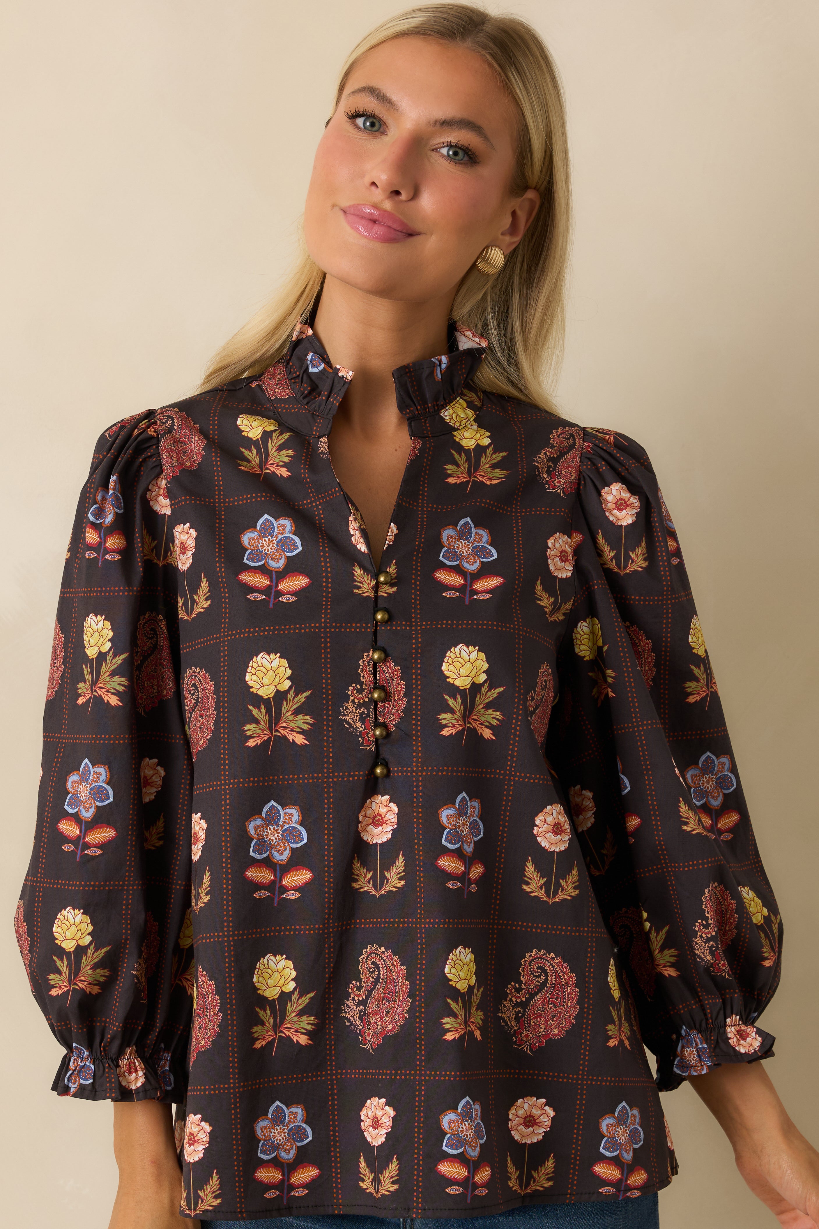 Close-up of the ruffled neckline and upper half of the blouse highlighting the floral print and metallic buttons.

