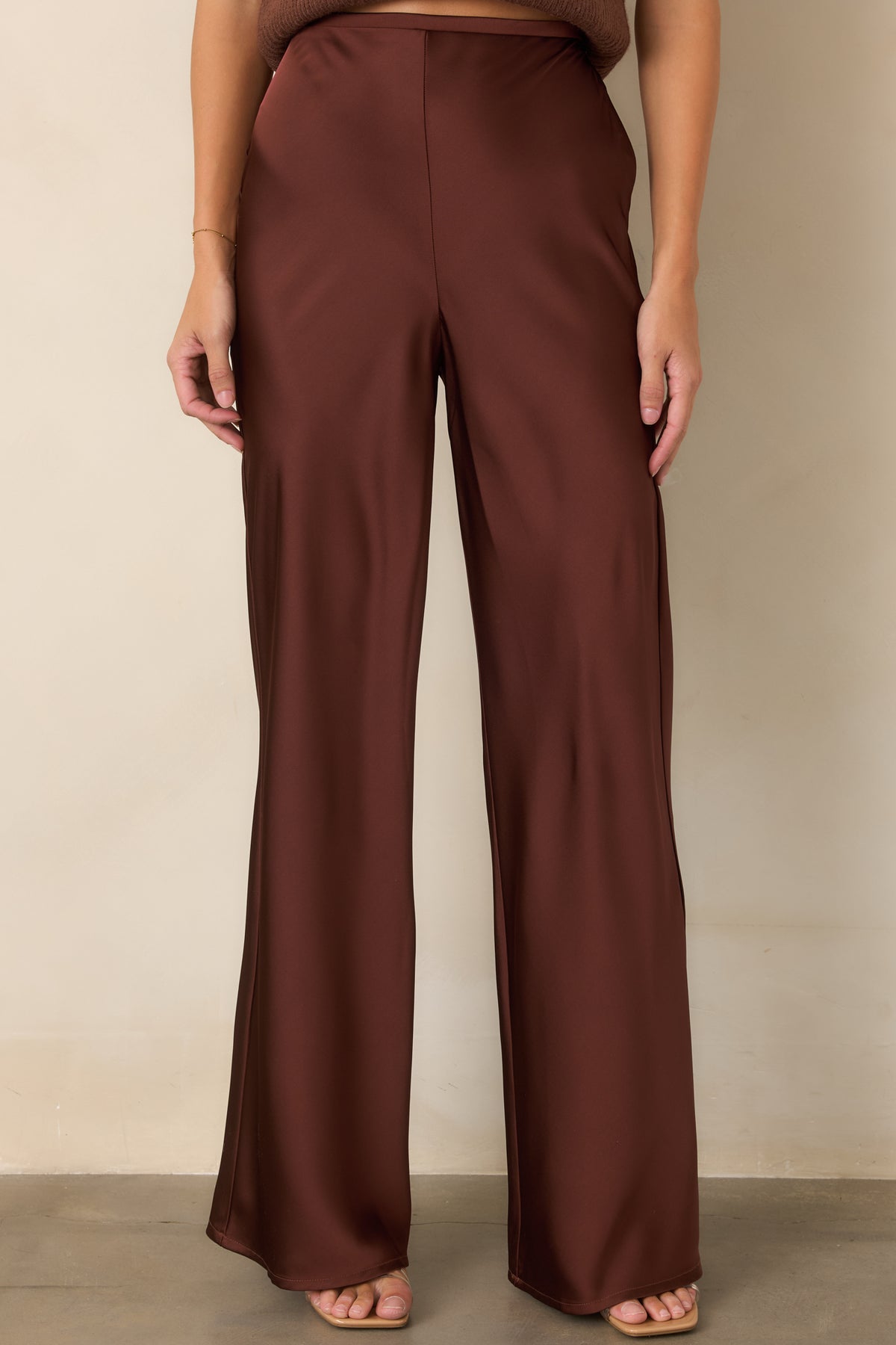 Rust brown satin pants highlighting the clean flat-front waistband, high-rise fit, and softly lustrous finish.