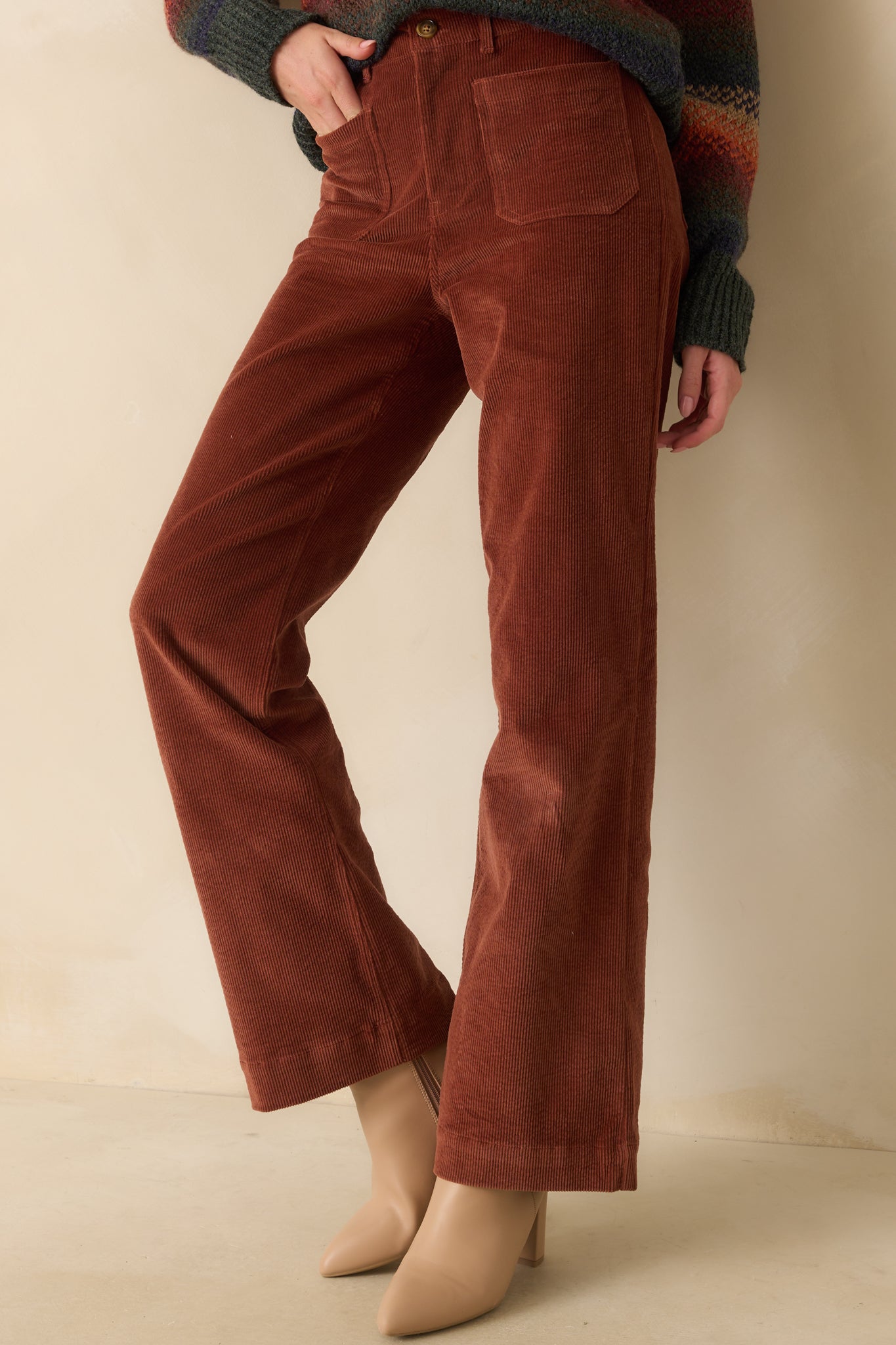 Close view of the high-rise waist and zip fly with button closure on rust corduroy pants.