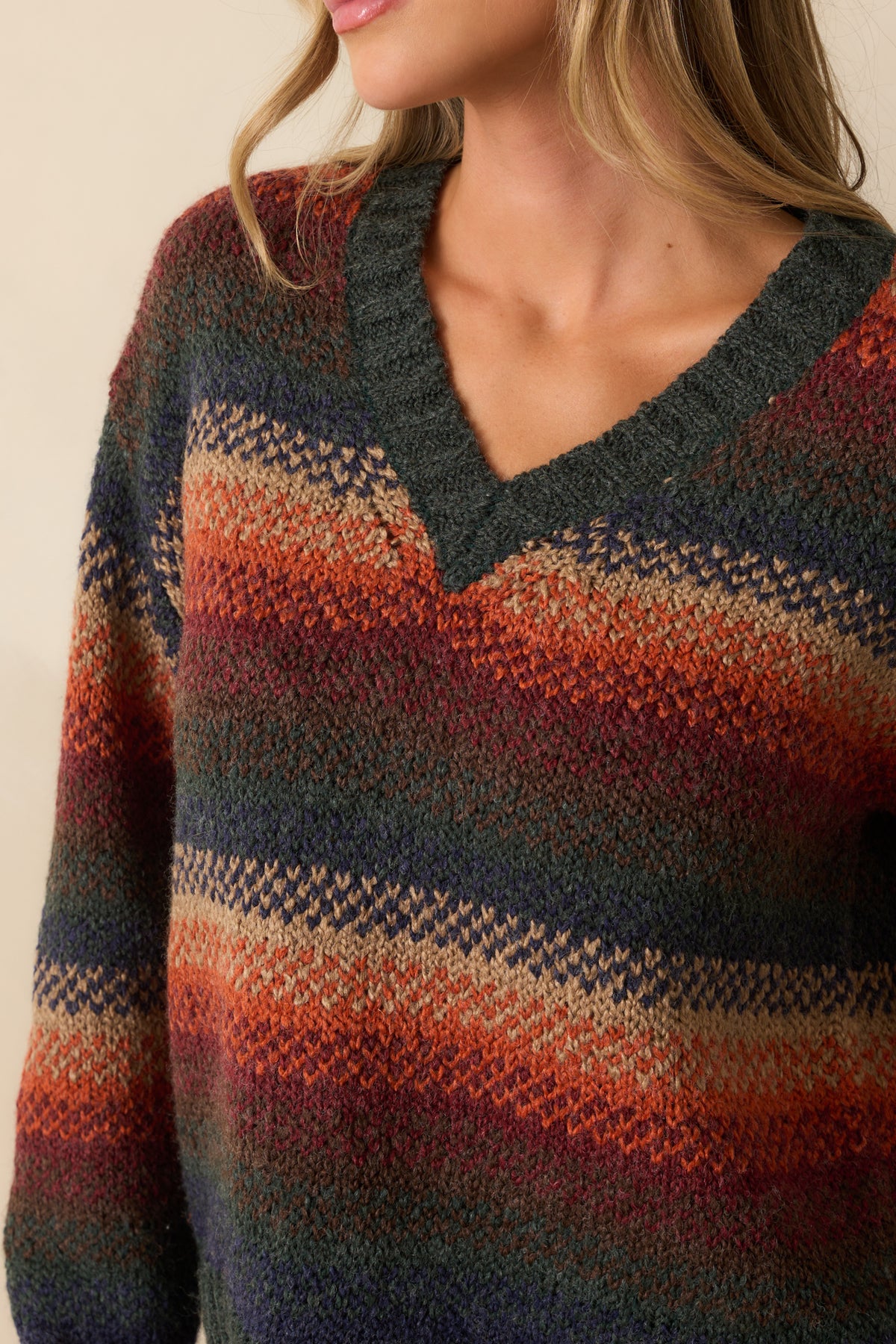 Close-up of rust knit sweater showcasing multicolor horizontal stripes and ribbed texture at neckline and cuffs.