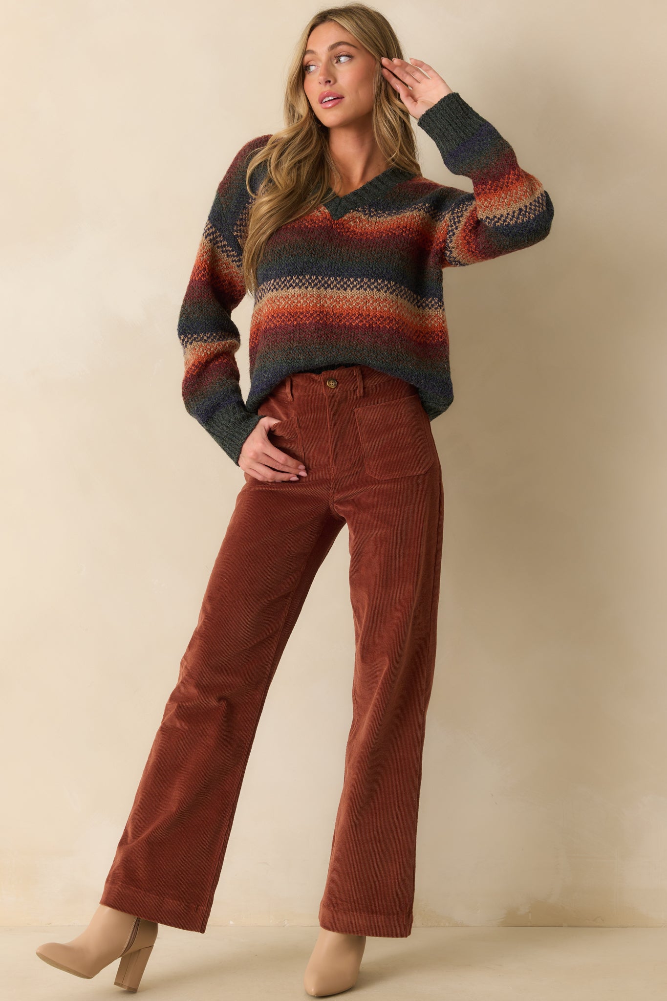 Rust knit sweater with multicolor horizontal stripes, V-neckline, ribbed cuffs and hem, shown in a relaxed front view.