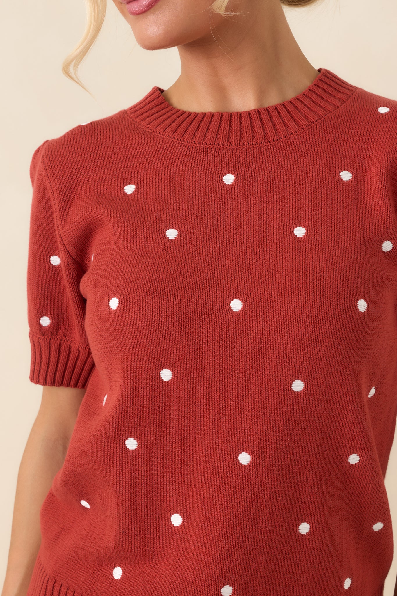 Close-up of the rust red cotton knit top showcasing the ivory polka dots, ribbed trim, and textured knit finish.