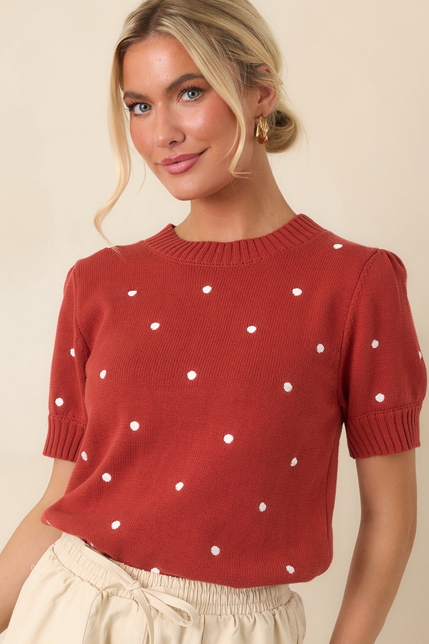 Close view of the rust red knit top highlighting the ivory polka dot pattern, ribbed crew neckline, and soft cotton texture.