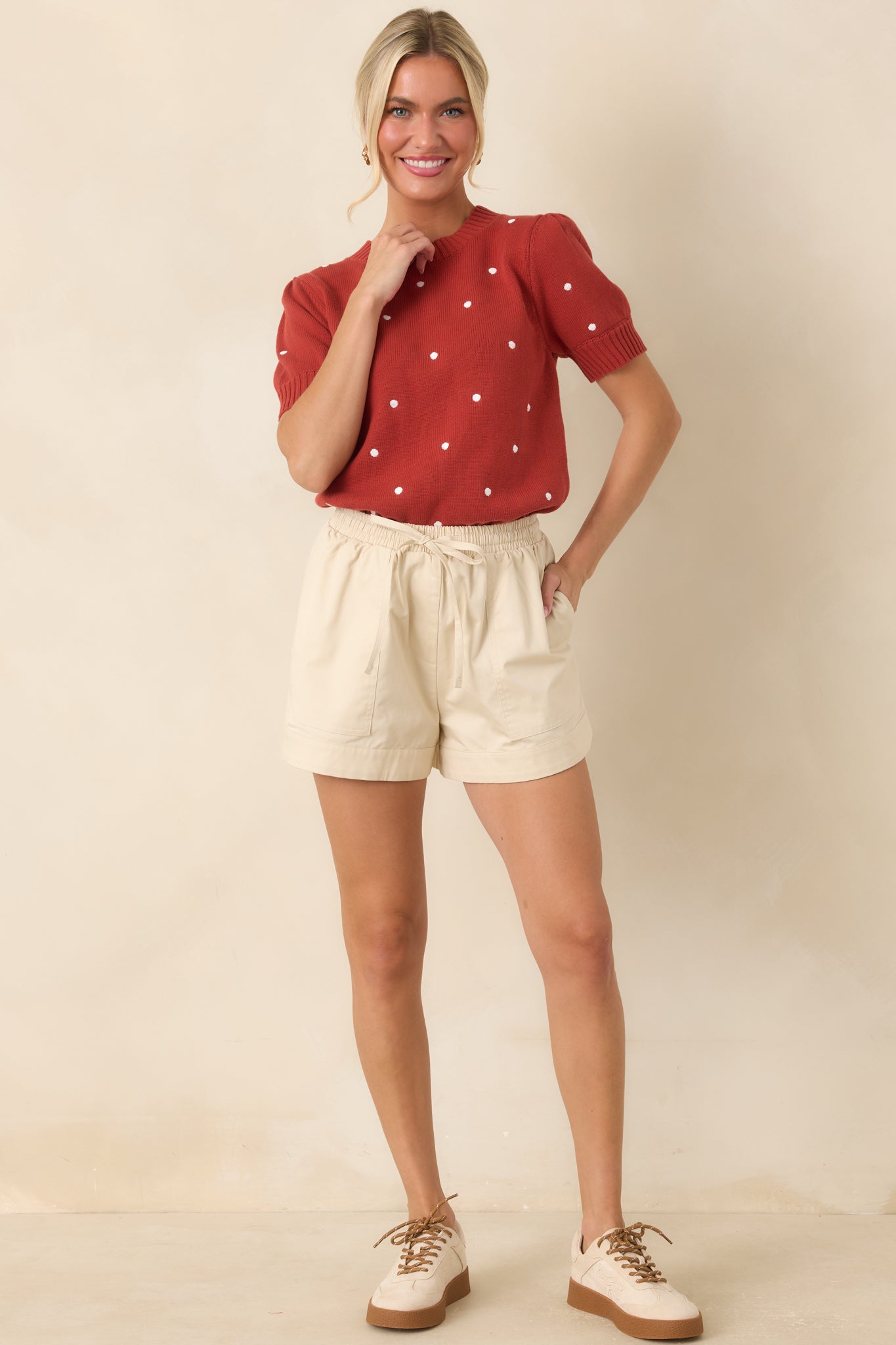 Rust red knit top featuring scattered ivory polka dots, short puff sleeves, ribbed trim, and a relaxed structured fit.