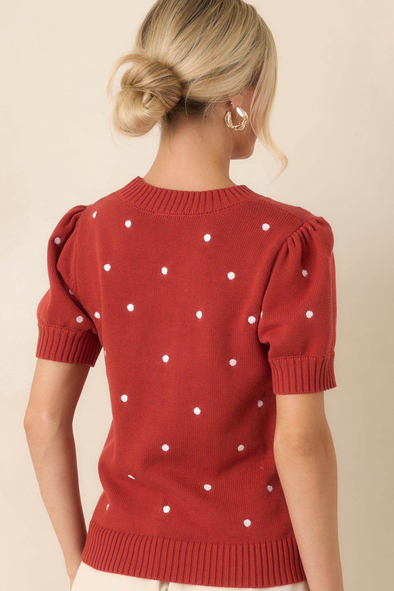 Rear view of the rust red cotton knit top featuring ivory polka dots, short puff sleeves, ribbed hem, and a clean back silhouette.