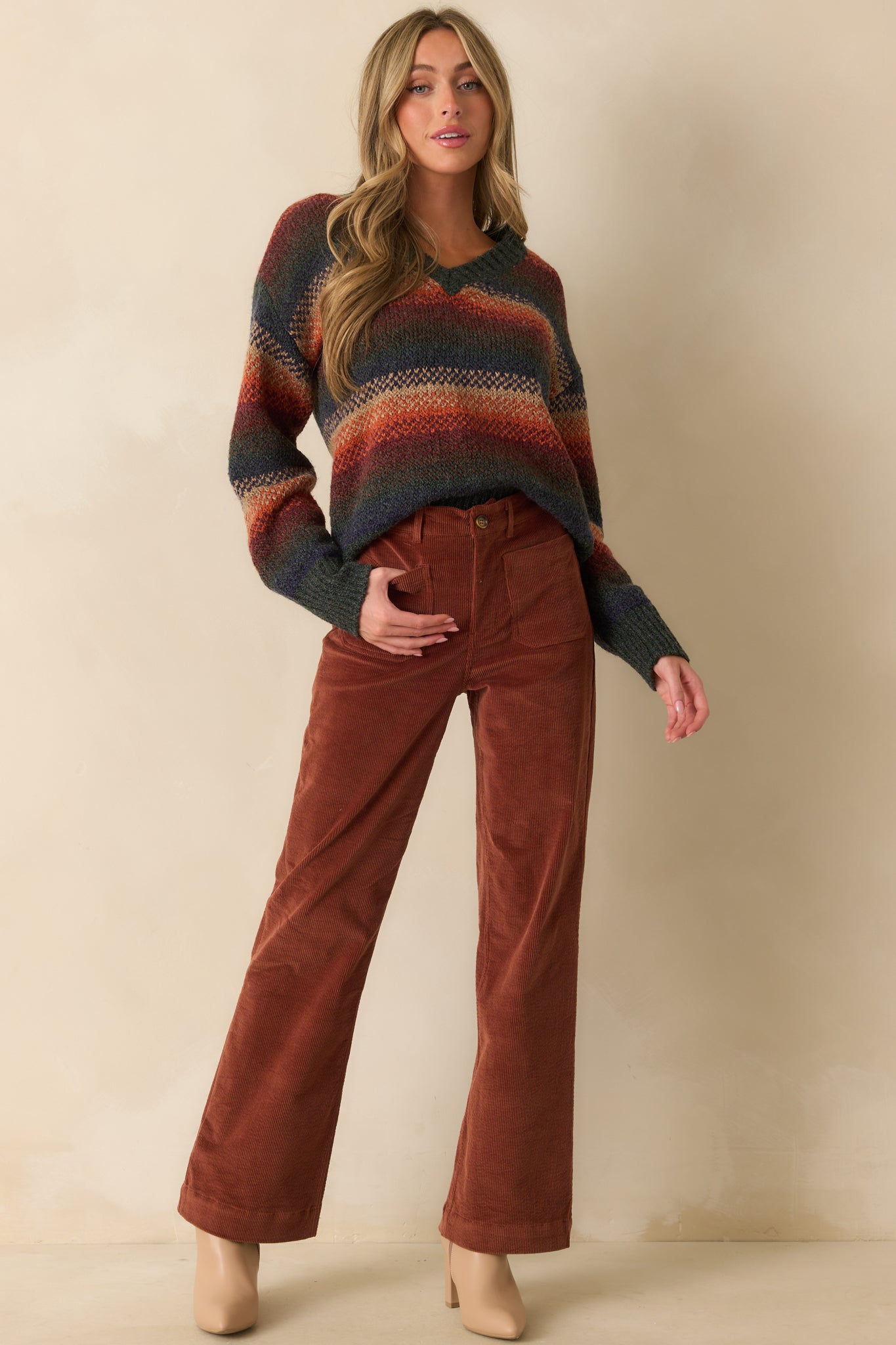 Front view of a rust sweater featuring long sleeves and colorful stripe pattern, with a ribbed hem and V-neckline.