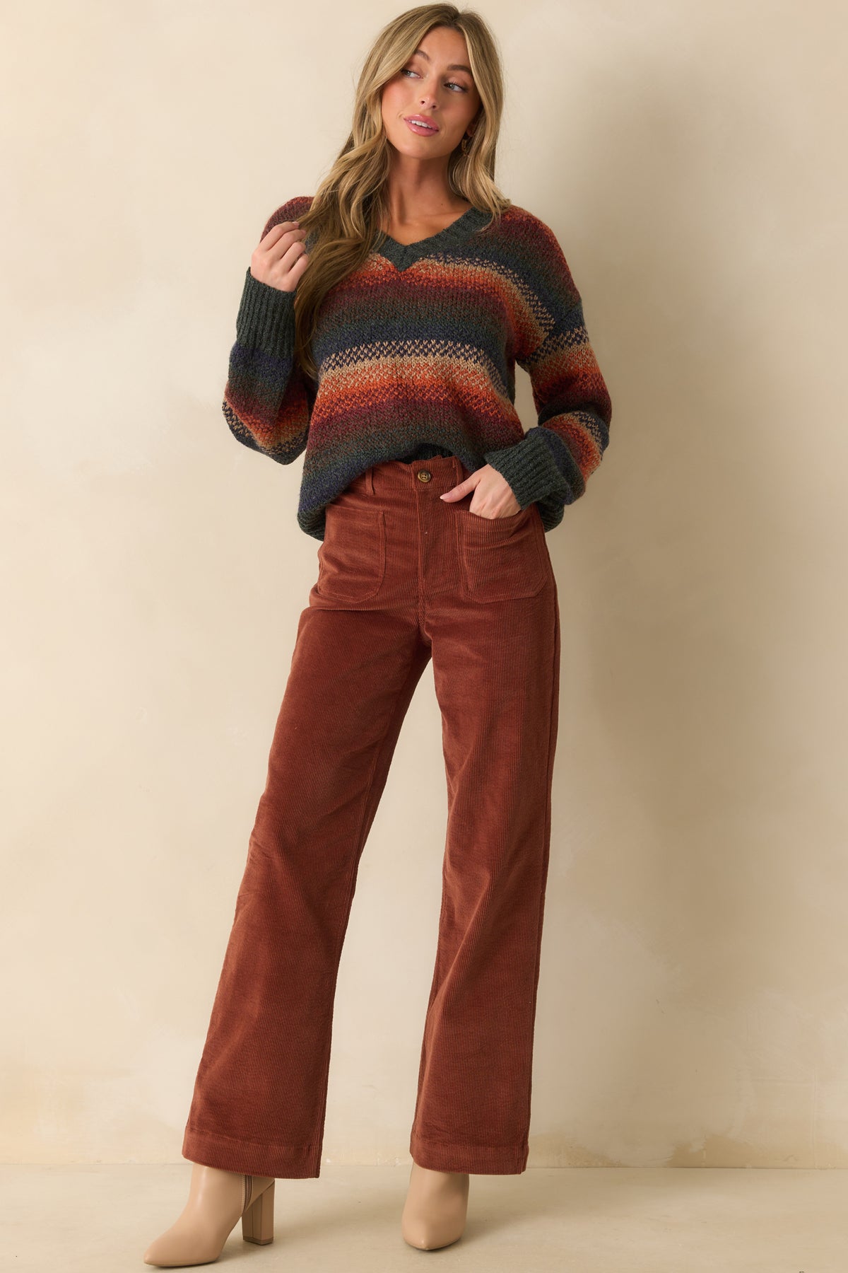 Relaxed rust sweater displaying horizontal multicolor stripes, ribbed cuffs and hem, and a V-neck, seen from the front.
