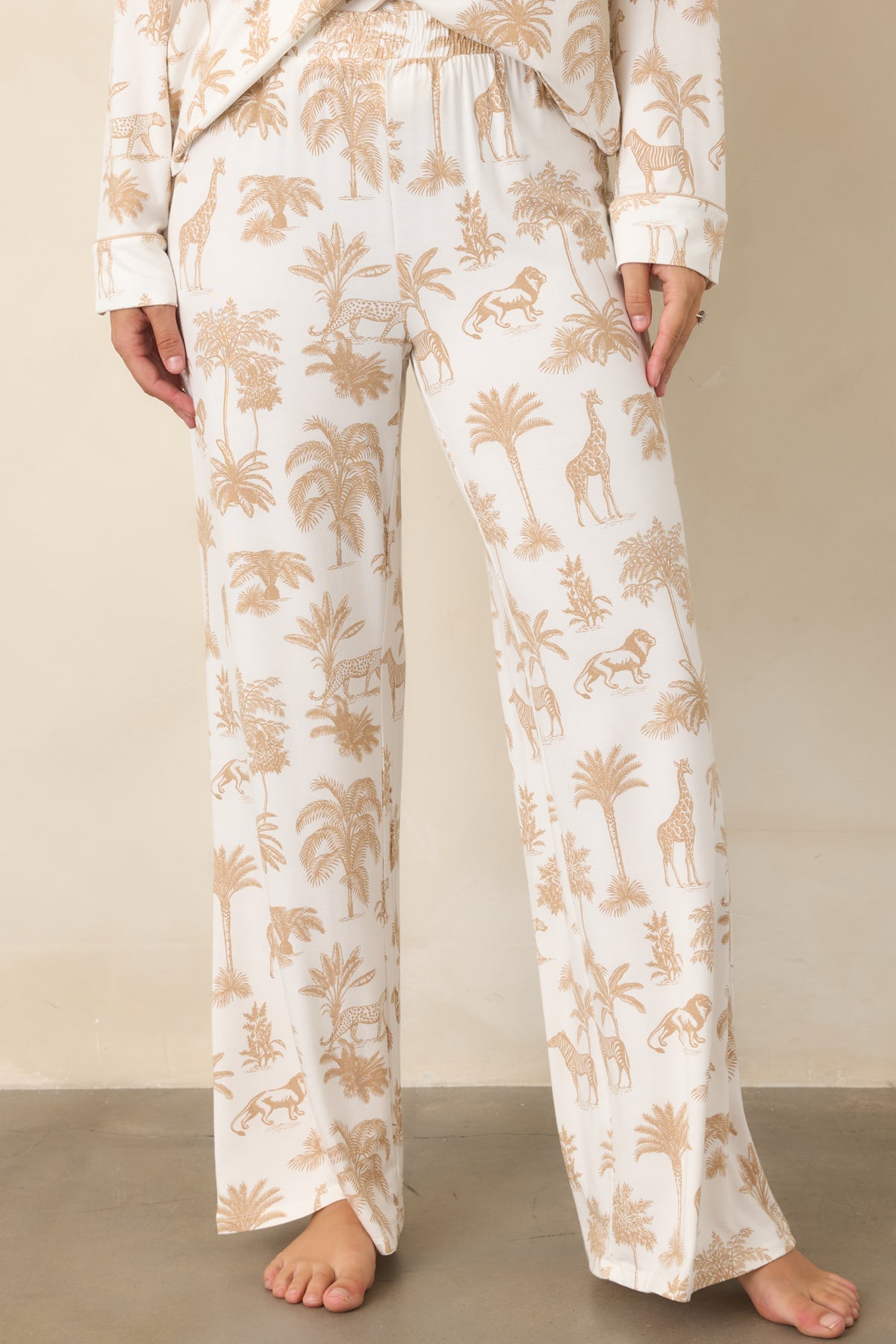 Safari animals and leafy tropical foliage decorate the ivory fabric, creating a playful scenic pattern across the relaxed pants.