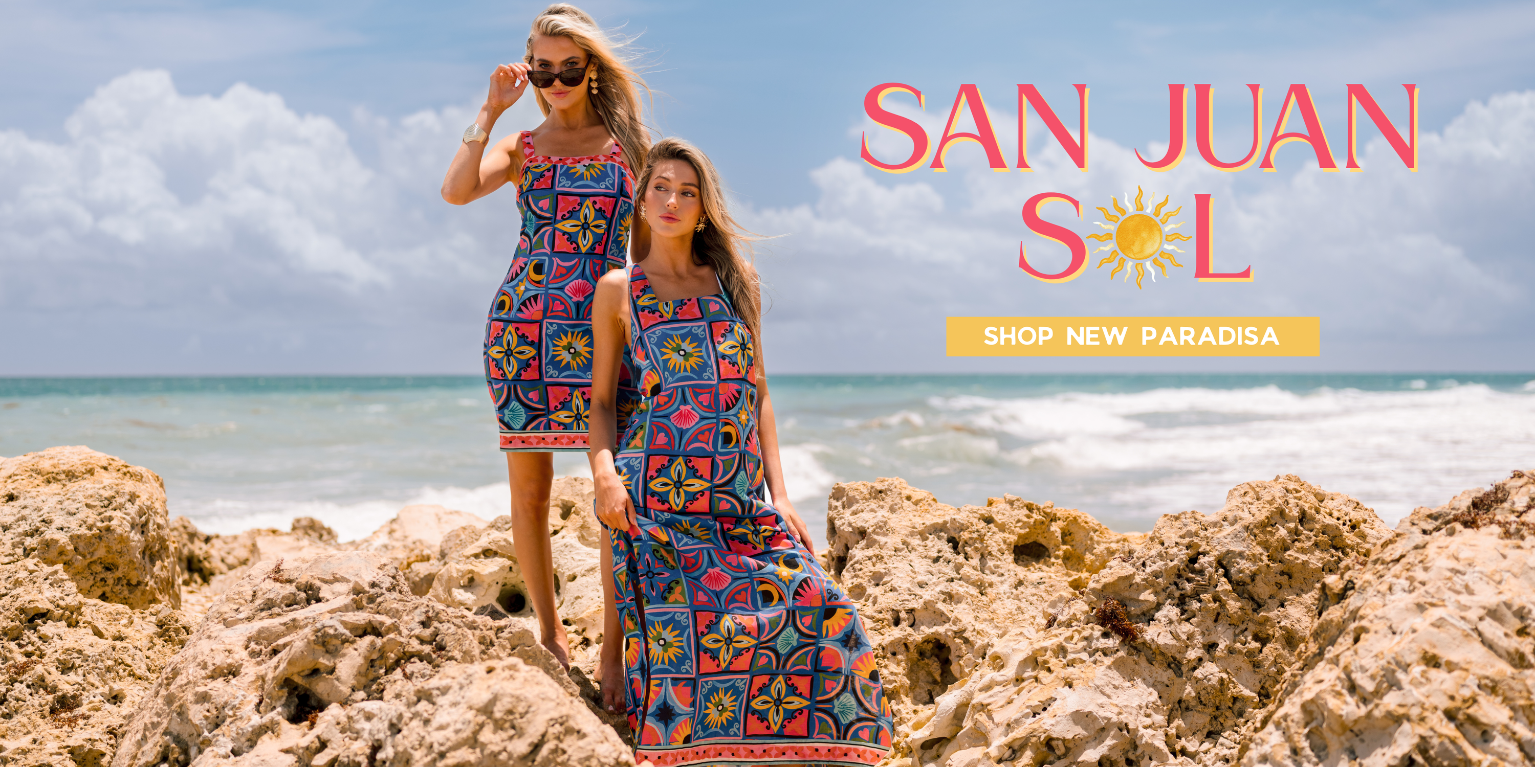 Two models in vibrant patterned dresses on a sunny rocky shoreline with ocean waves in the background. The image features “San Juan Sol” text across the top and a “Shop New Paradisa” call-to-action button at the bottom.