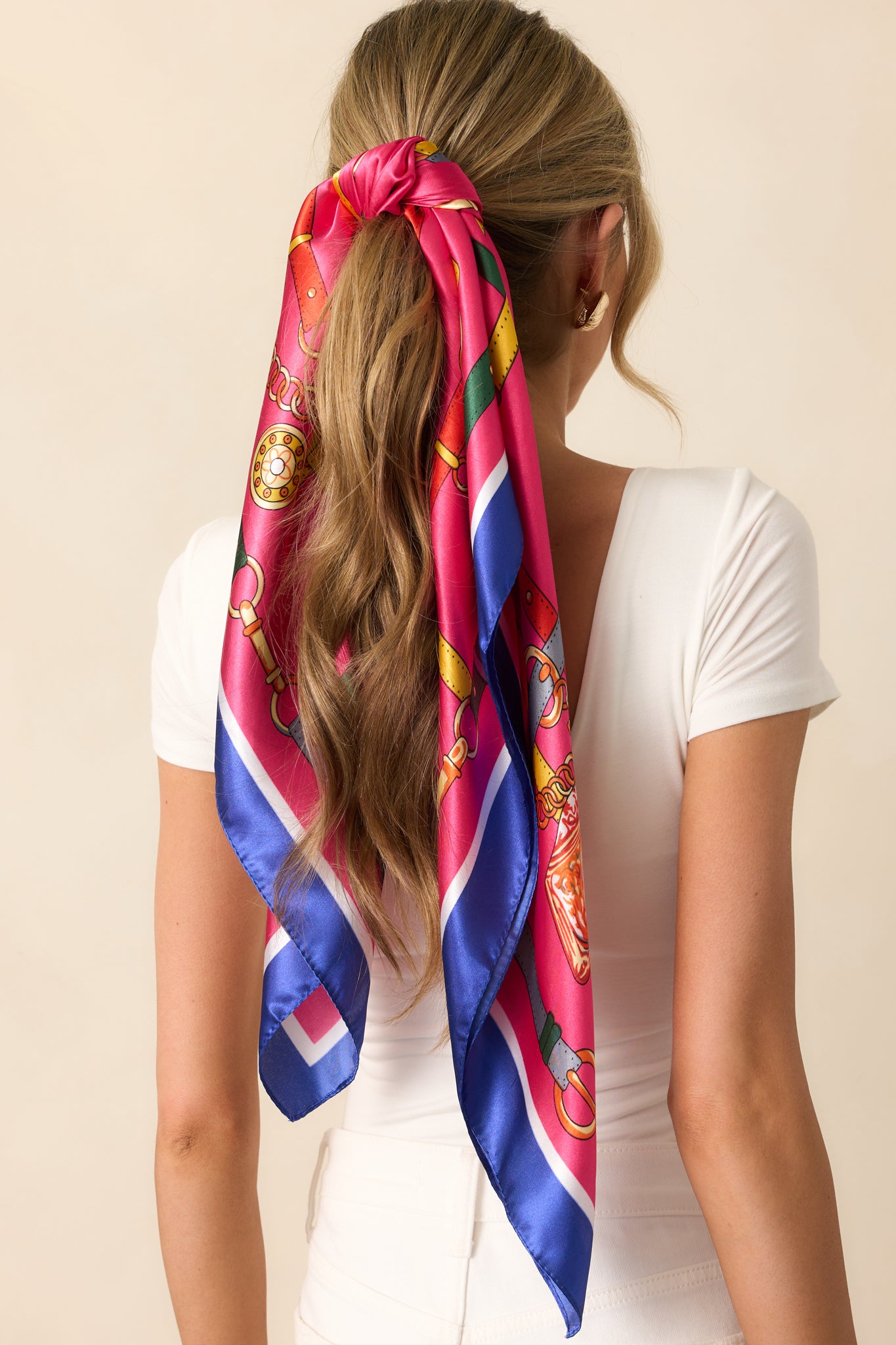 A satin fuchsia scarf featuring a bold multi-color print with a chain handbag strap design. The print is accented with vibrant shades of orange, red, white, and navy, creating a lively contrast.