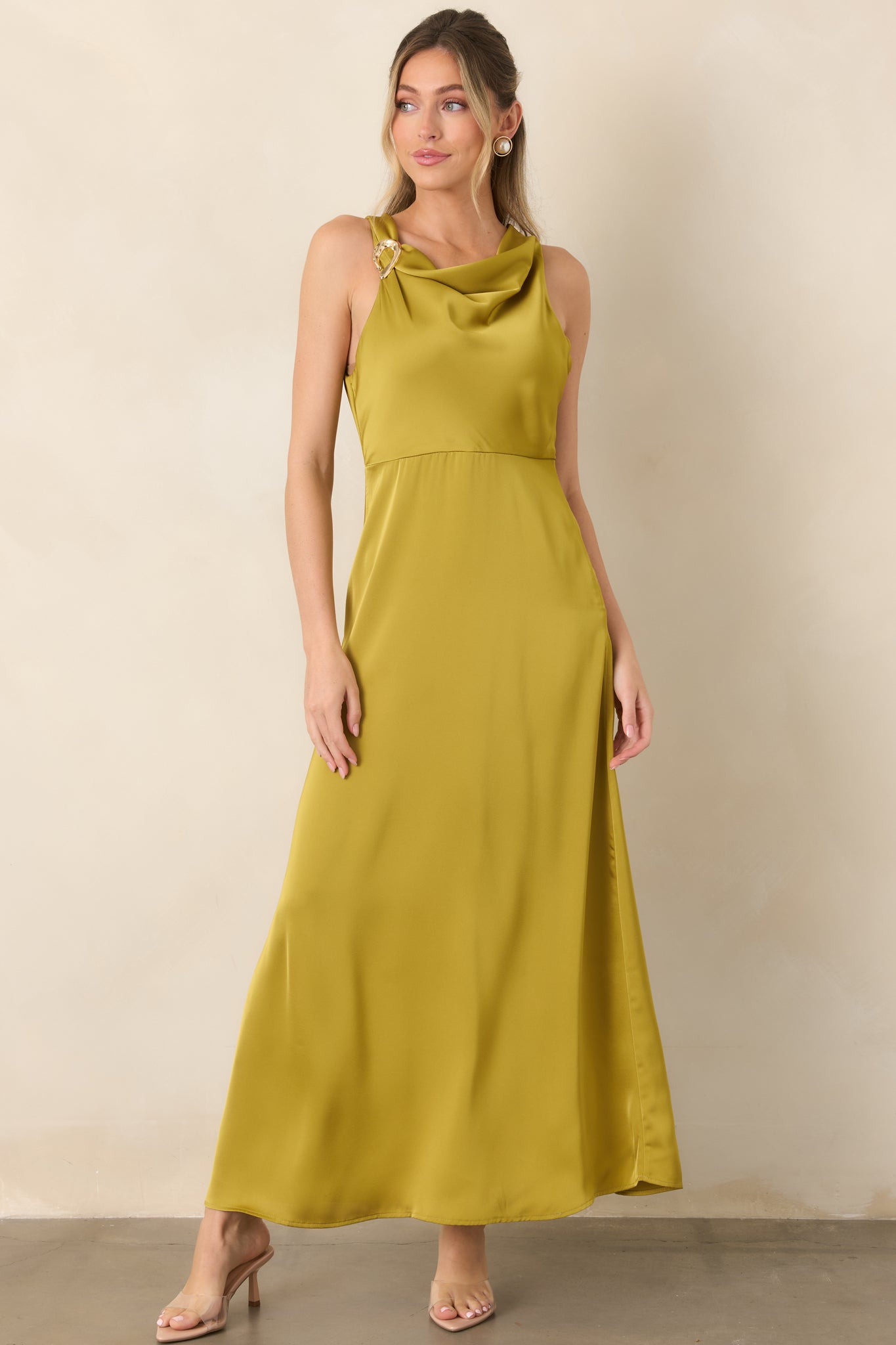 Satin maxi dress showcasing its softly gathered neckline, sculptural gold-tone shoulder accent, empire waist, and fluid floor-length skirt.