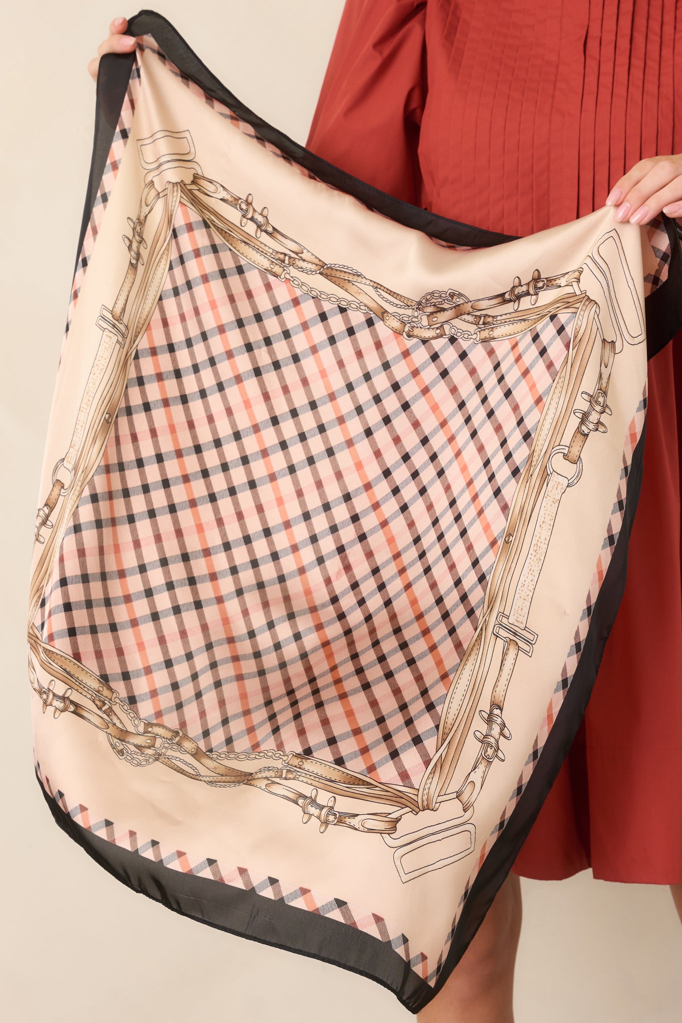 Detailed view of the silky satin scarf highlighting its neutral plaid center and ornate border of equestrian motifs.