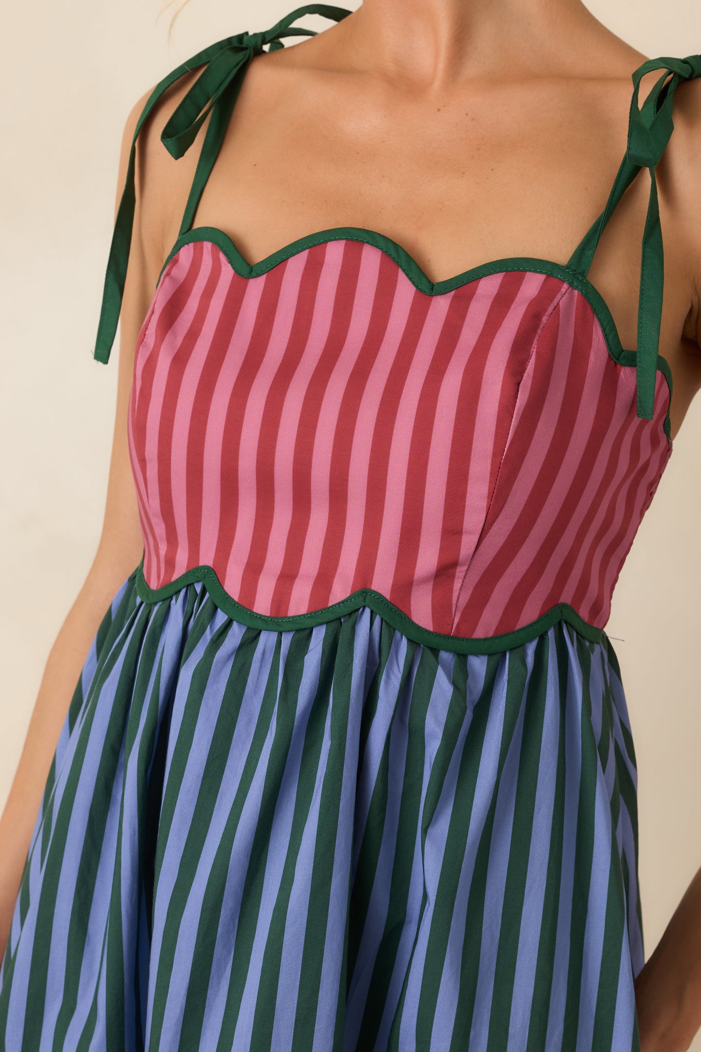 Close-up of the scalloped bodice featuring contrast piping, rosy tones, and detailed striped fabric.