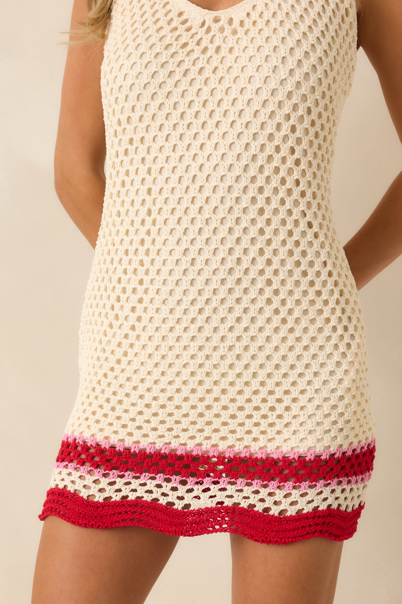 Close-up of the scalloped crochet hem with red stripe detailing on the ivory dress.