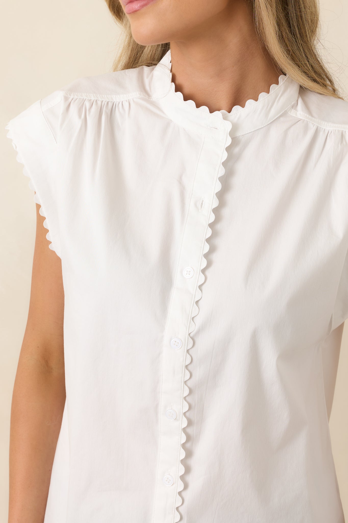 Scalloped trim on neckline, placket, and cap sleeves with stitched detailing.